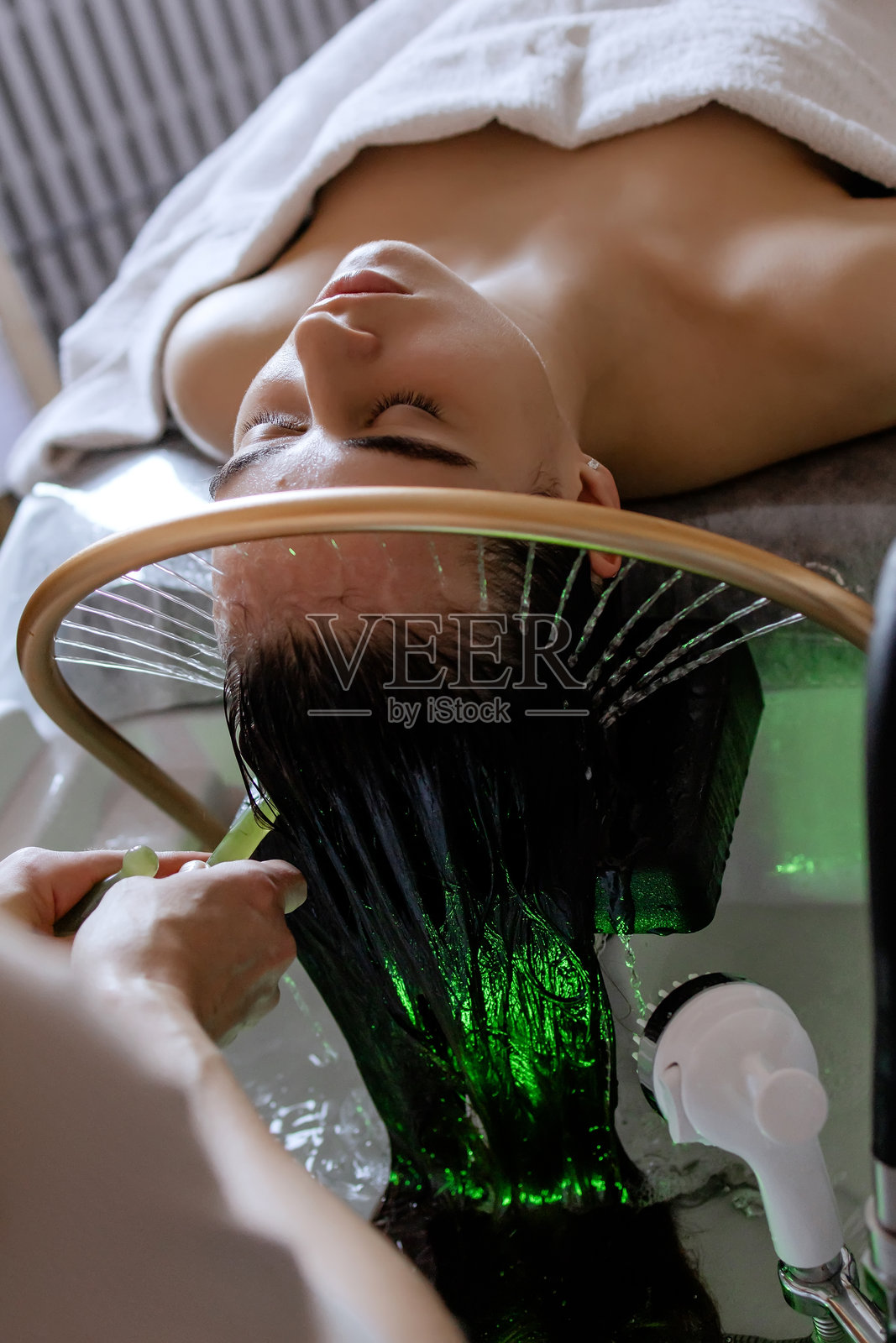 一位女性在美容院接受放松的日本头部水疗，绿色按摩棒轻轻放在她的头皮上，水从特殊工具中缓缓流出。照片摄影图片
