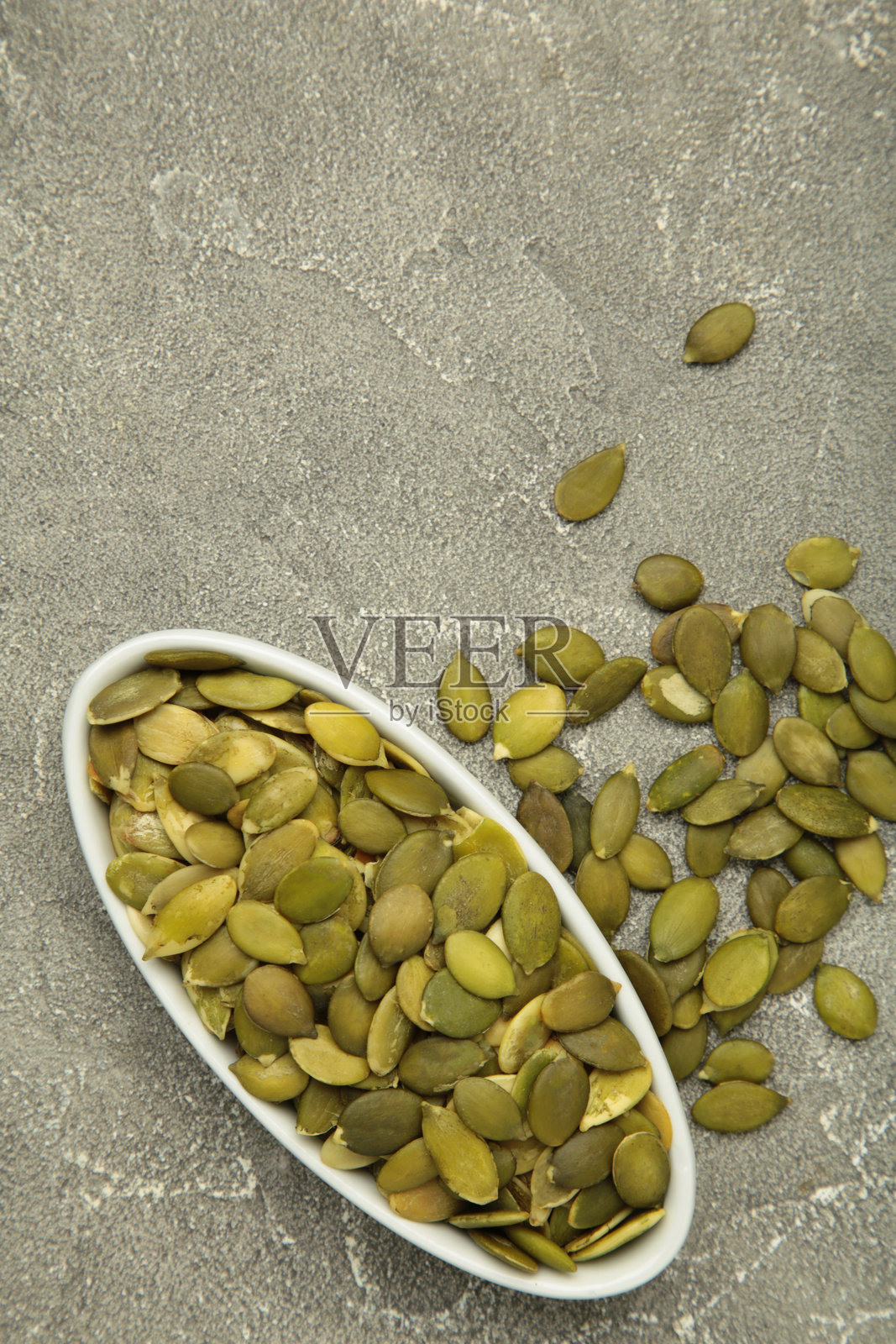 灰色混凝土背景上白色盘子里的南瓜子。照片摄影图片