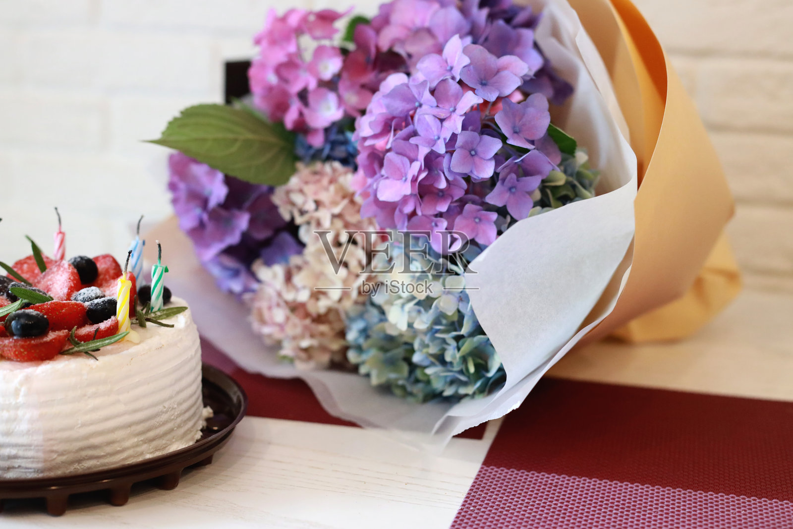 五彩缤纷的绣球花花束放在桌子上，旁边是一块草莓蓝莓生日蛋糕。贺卡照片摄影图片