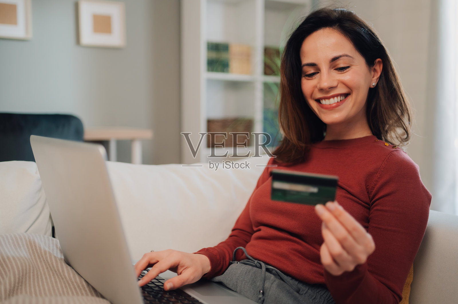 微笑的女性在家沙发上使用笔记本电脑和信用卡进行在线购物照片摄影图片