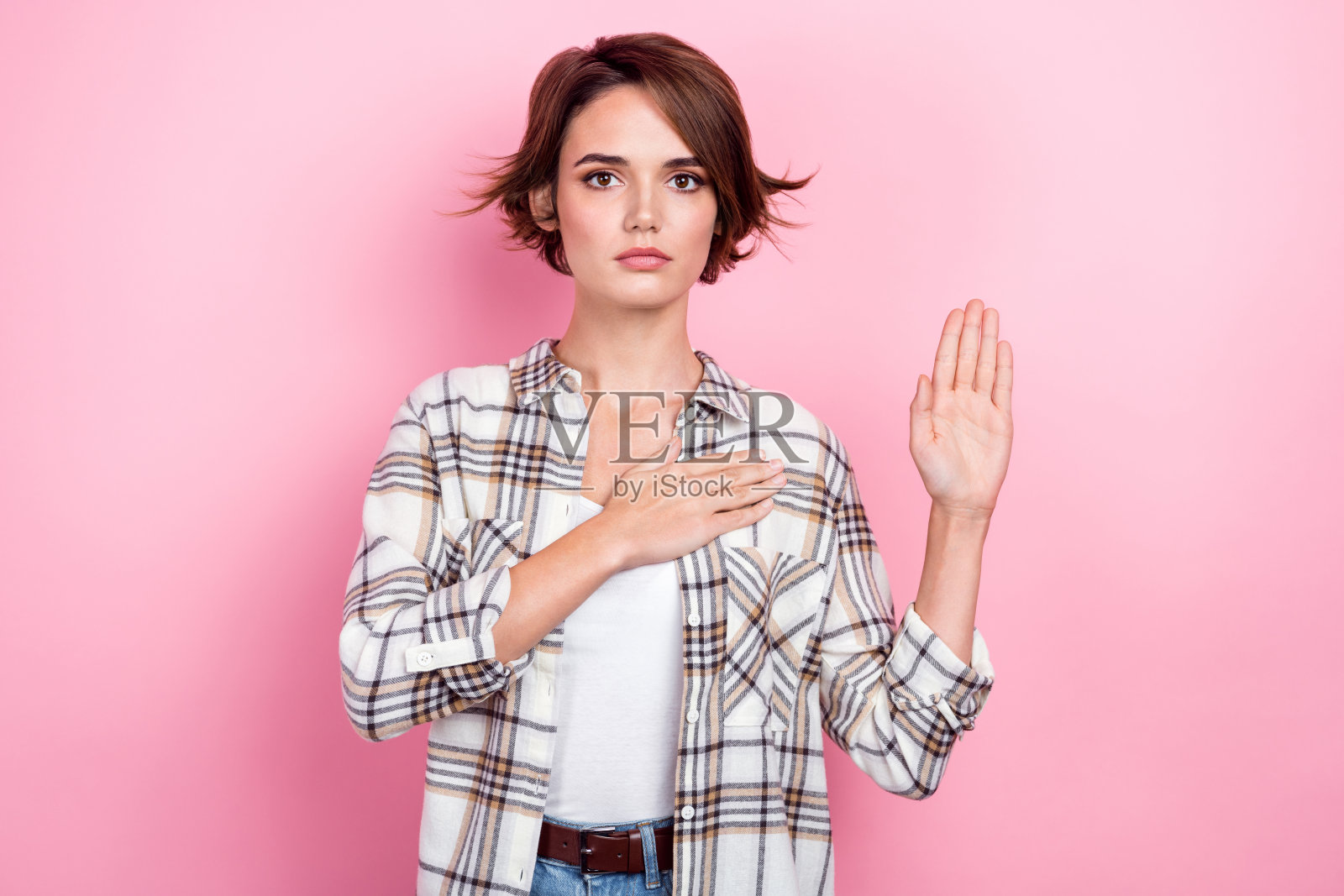 宁静美丽的人物肖像，手臂触碰心脏，手掌抬起许下承诺，背景为粉色。照片摄影图片