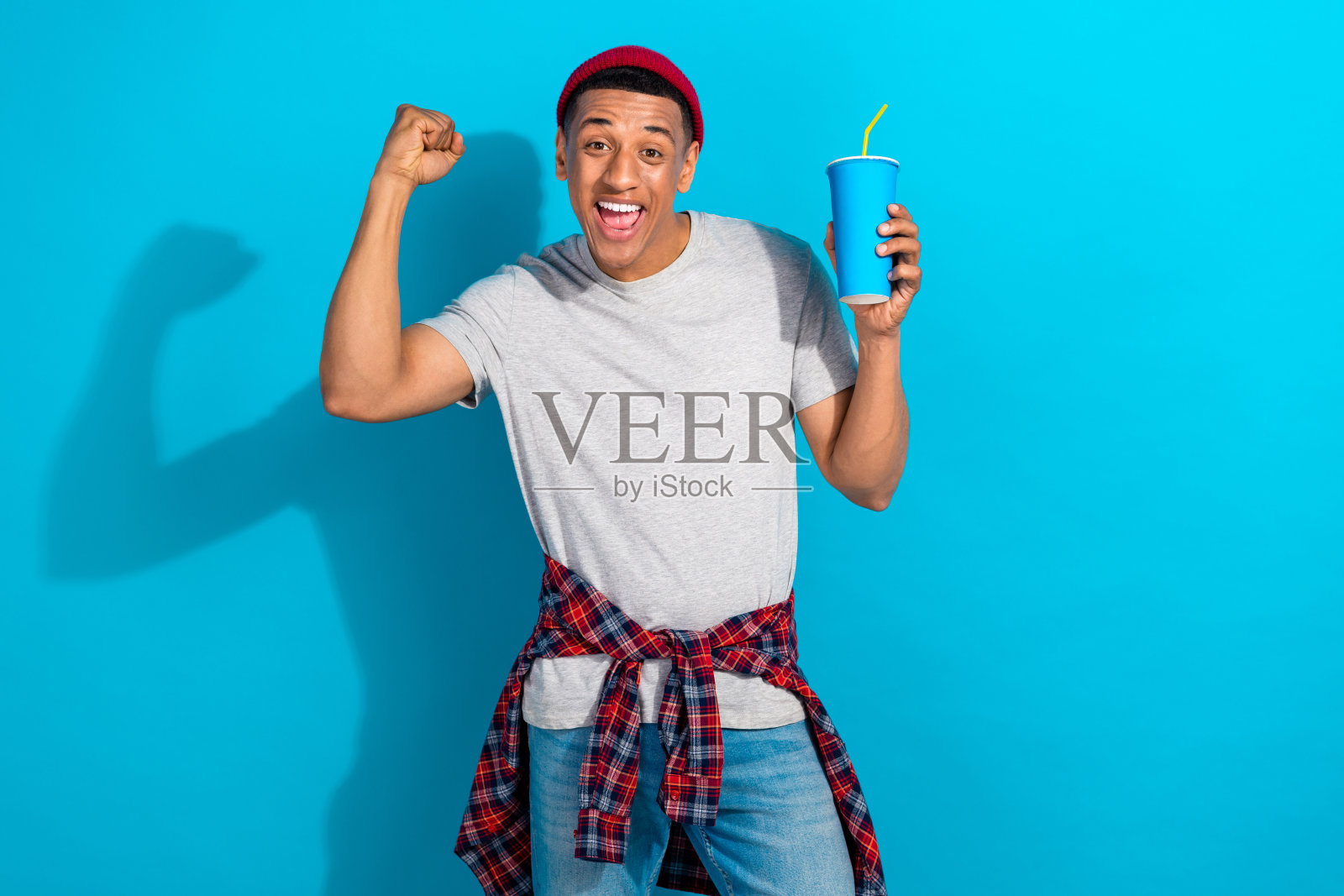 兴奋的时尚人士手持汽水杯，举起拳头，系着前襟衬衫，背景为蓝色。照片摄影图片