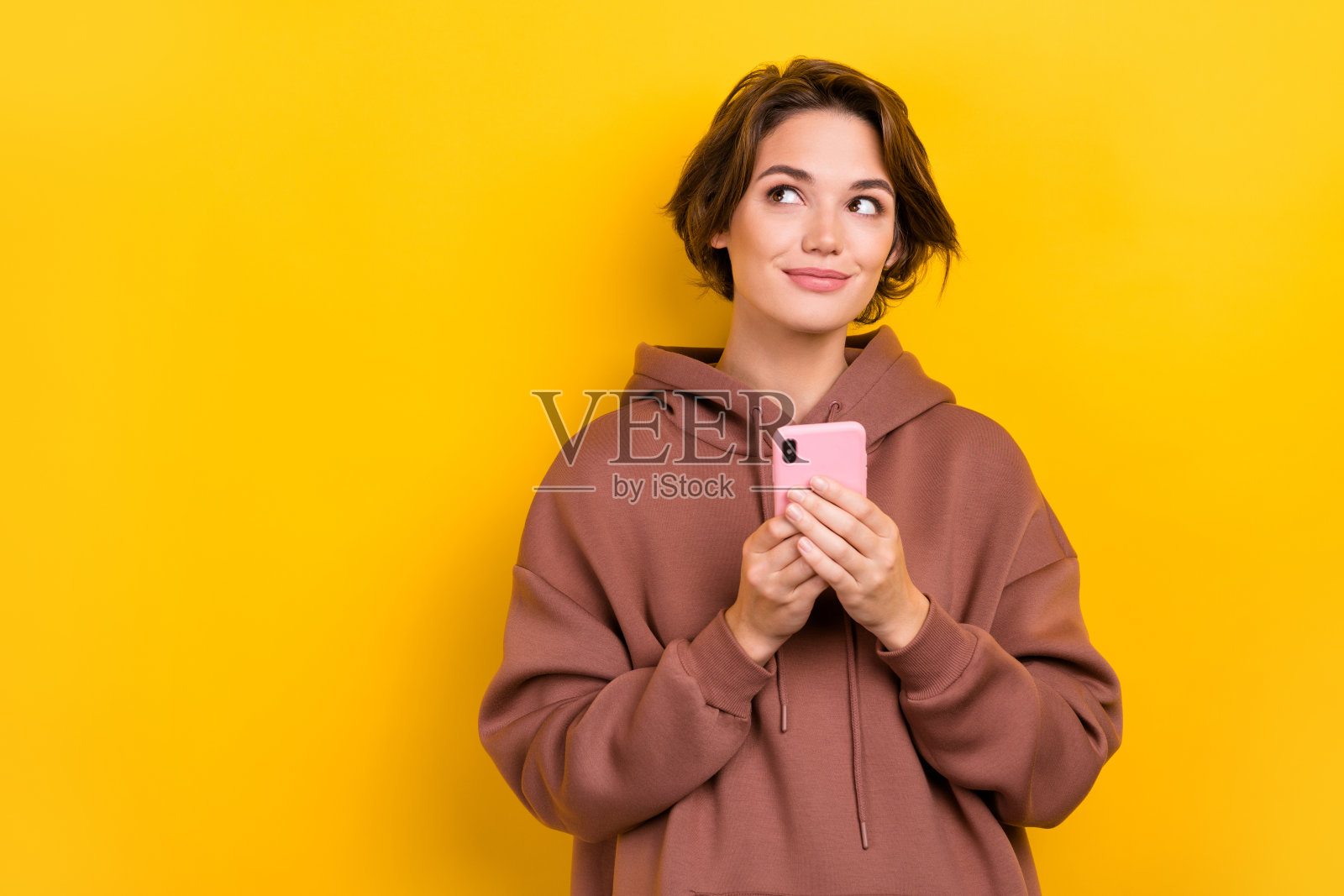 迷人的女孩手持智能手机，目光空灵，背景为黄色。照片摄影图片