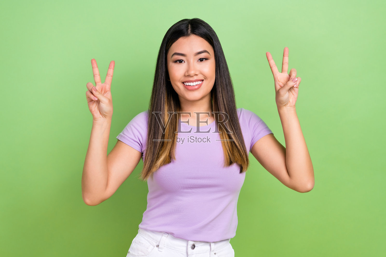 漂亮的越南华裔年轻女孩在绿色背景下穿着时尚的紫色服装，做出双V手势的照片肖像照片摄影图片