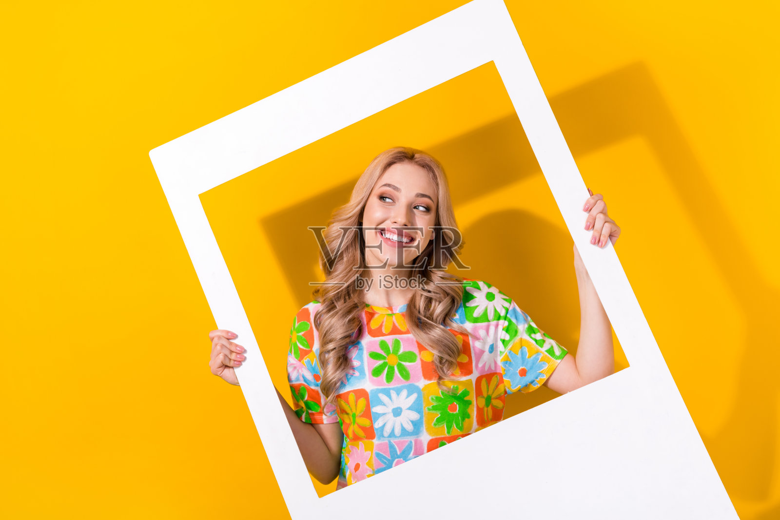 心情愉快的可爱女孩，波浪卷发，穿着彩色T恤，望向相框外的空白空间，背景为黄色。照片摄影图片