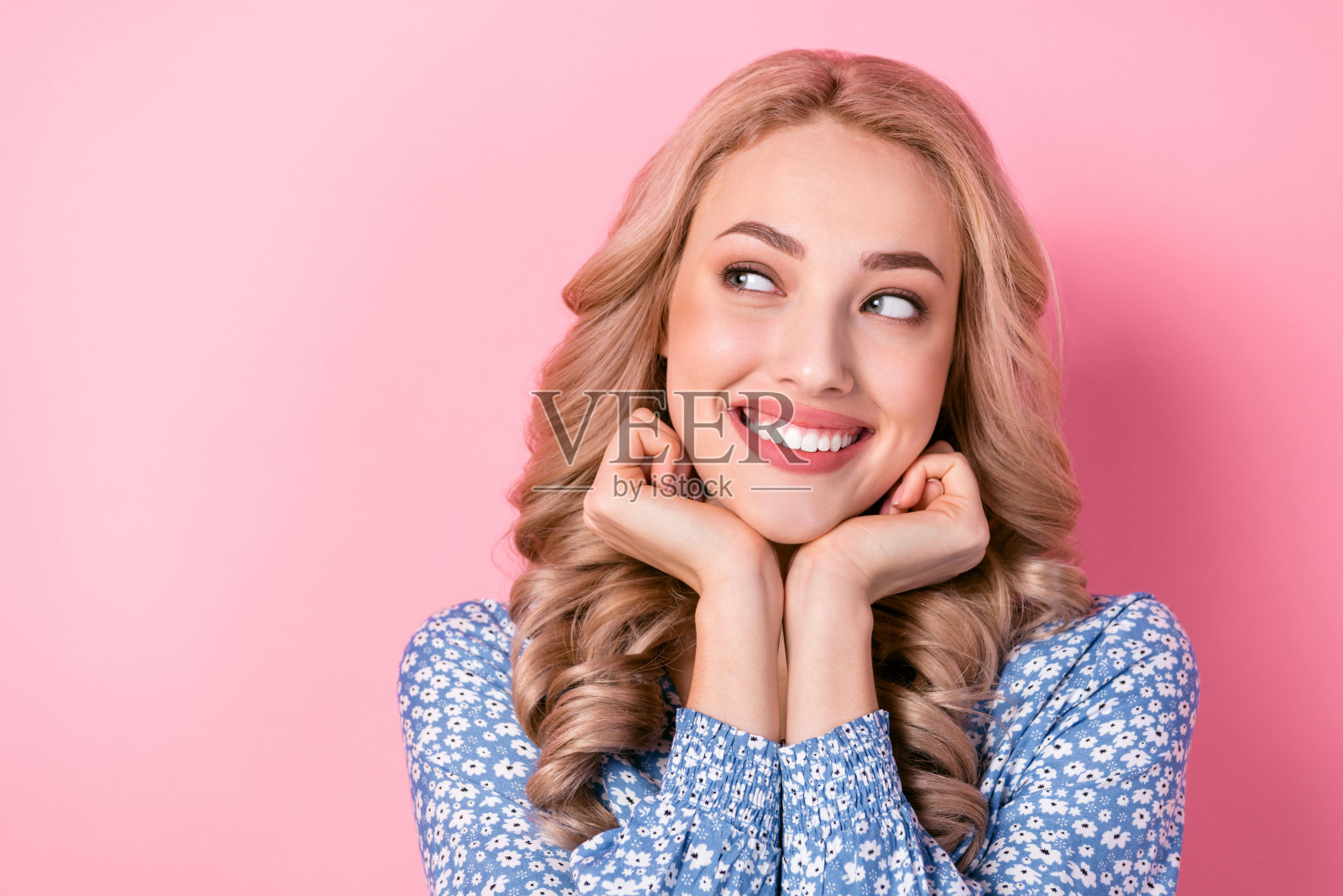 可爱的迷人女友，金色波浪长发，手轻触脸颊，沉思的想象，背景为粉色。照片摄影图片