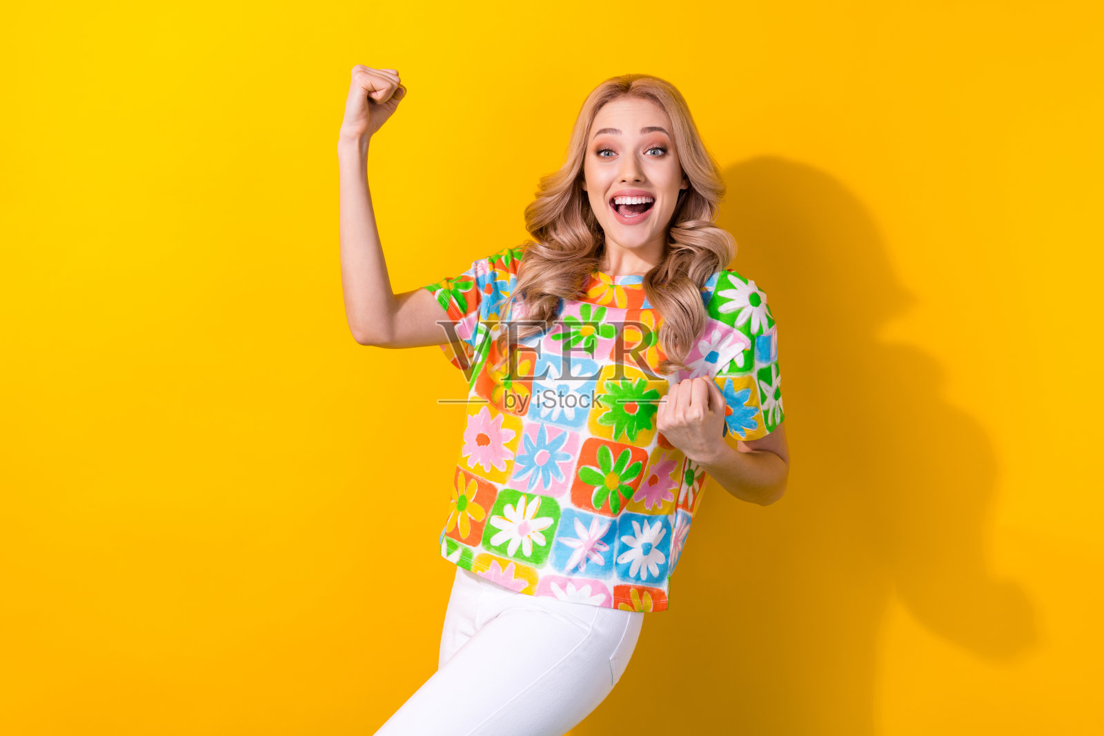 一位迷人的兴奋女士在黄色背景下举起拳头，欢呼“耶”，庆祝体育比赛的结果。照片摄影图片