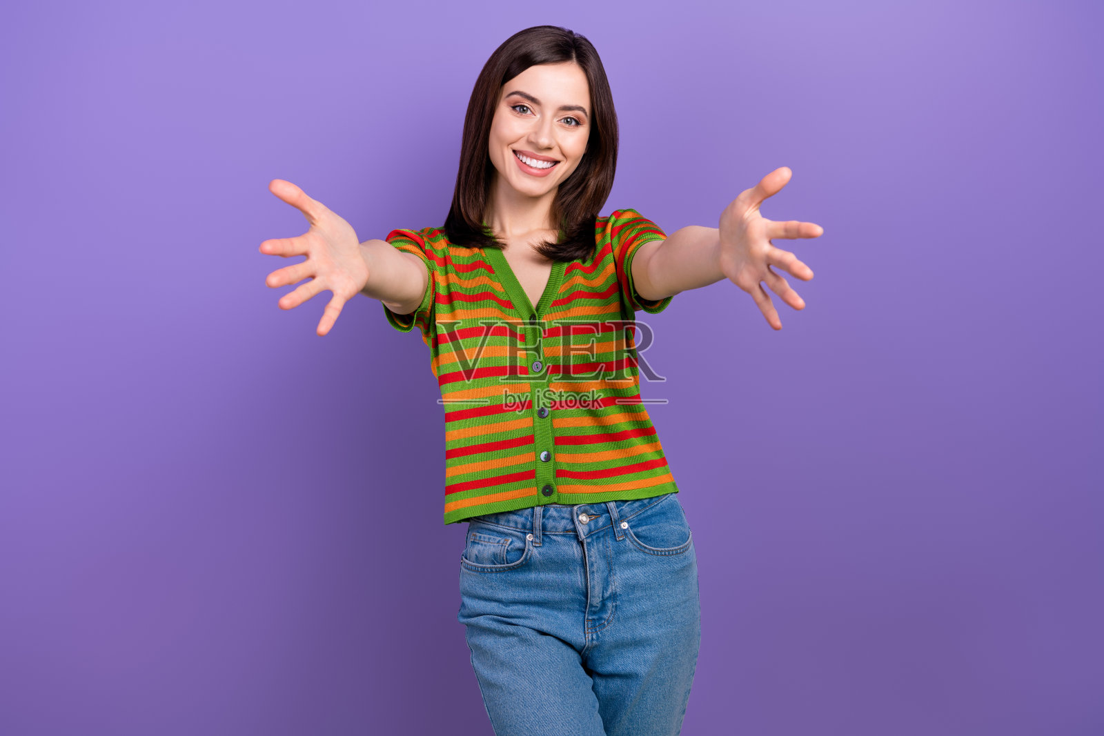 心情愉快的可爱女孩，时尚发型，穿着条纹开衫，伸出双臂向你拥抱，背景为紫色。照片摄影图片