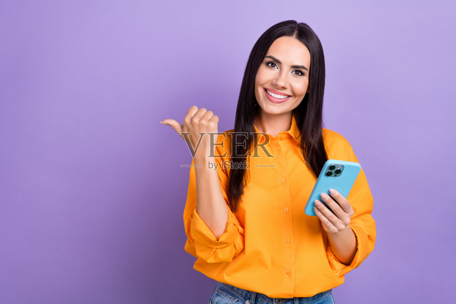 年轻快乐的女企业家使用智能手机，手指指向空白处，快速的WiFi用户，背景为紫色。照片摄影图片