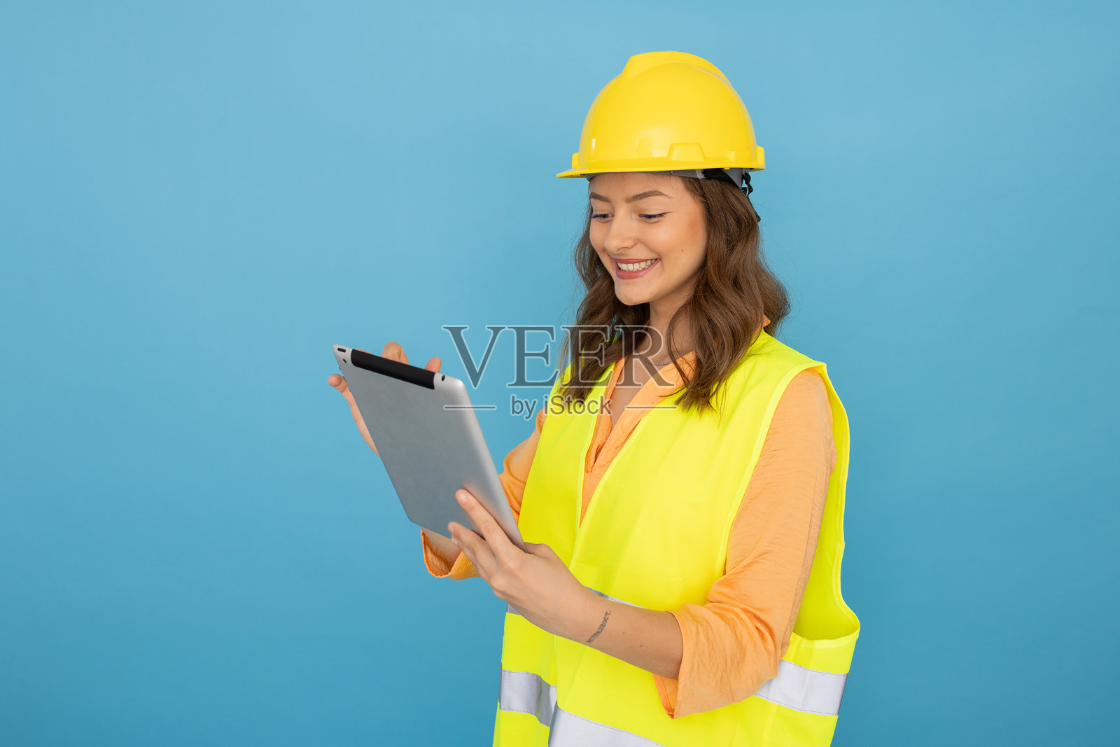 年轻建筑师戴着安全头盔和背心，在蓝色背景下使用数字平板电脑照片摄影图片