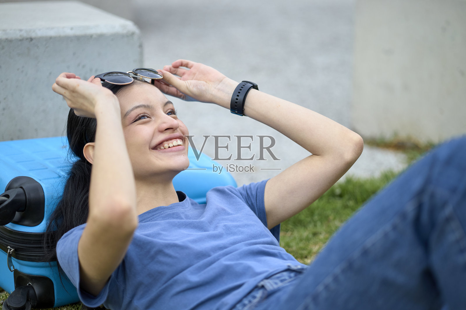 微笑的旅行者躺在行李箱上，玩弄着太阳镜照片摄影图片