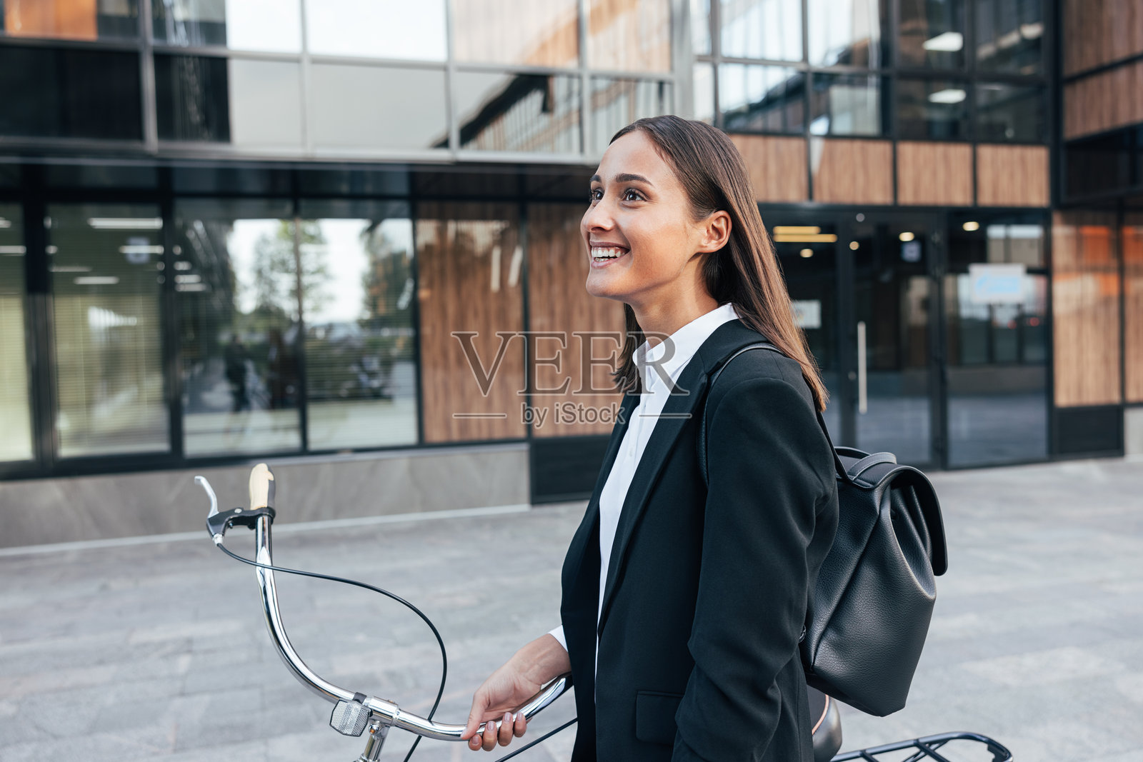快乐的女性背着背包骑自行车在户外行走。年轻微笑的女商人在街上骑自行车。照片摄影图片