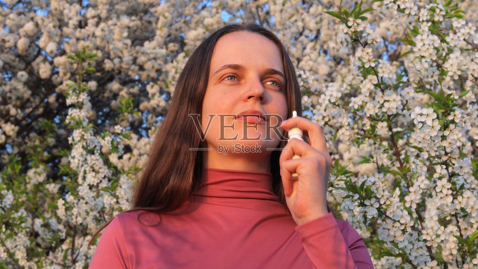 一位女性站在鲜艳的白色花朵中，在明亮的春日里使用产品缓解过敏症状。照片摄影图片