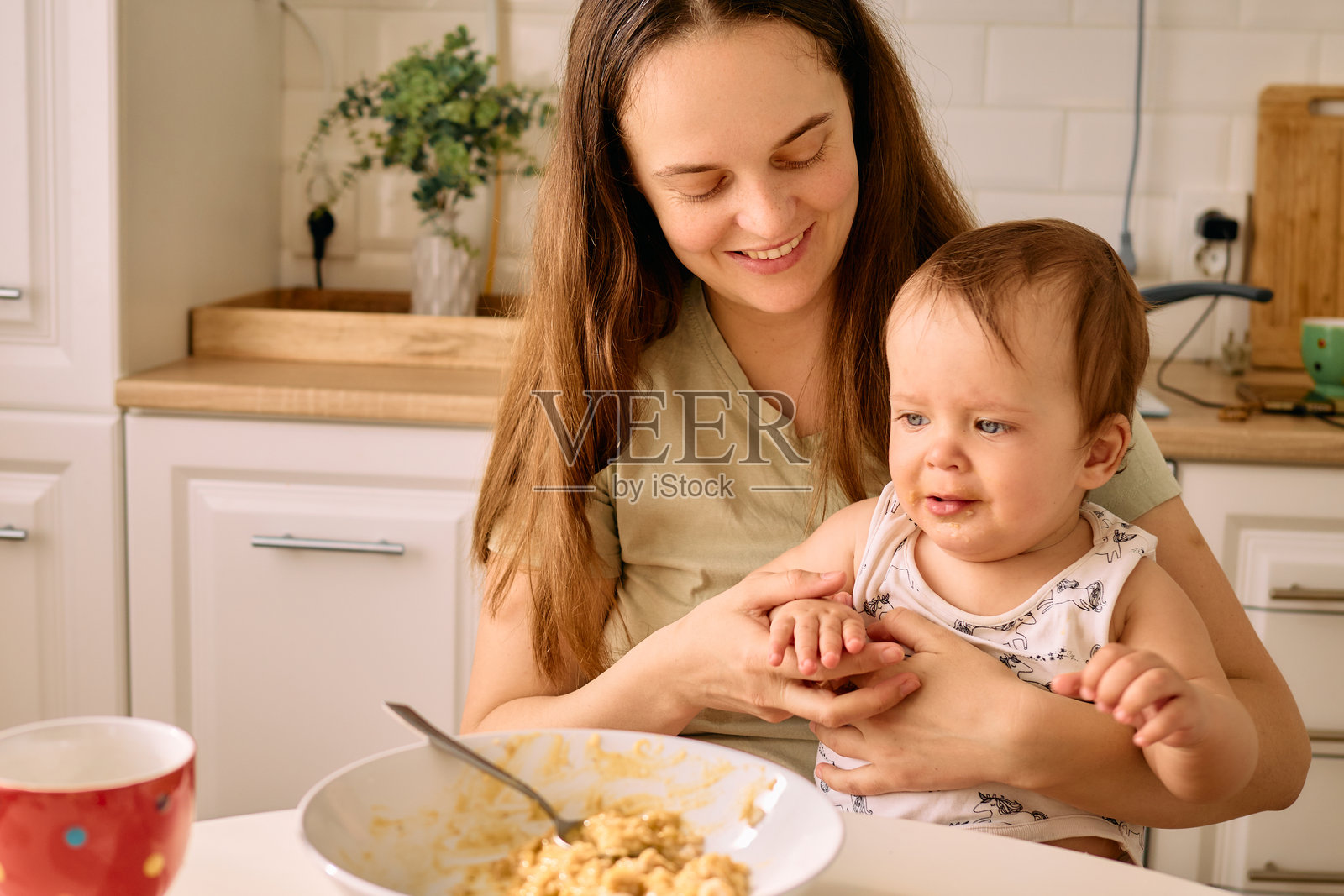 一位母亲在明亮的厨房里与她的宝宝分享快乐时光，愉快地互动，一起在桌子上享用早餐。照片摄影图片