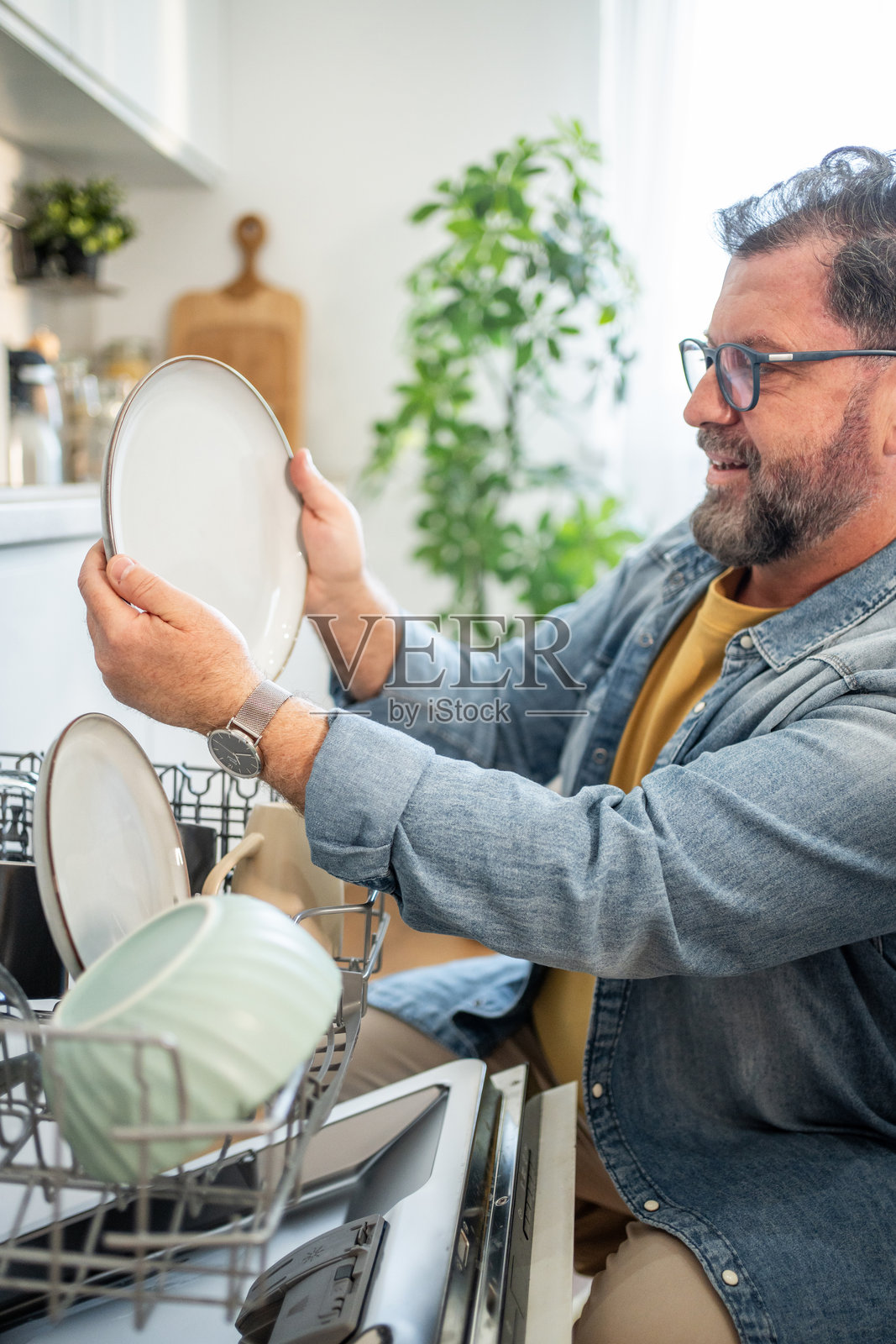 微笑的男人在现代厨房中从洗碗机里卸下干净的碗碟照片摄影图片