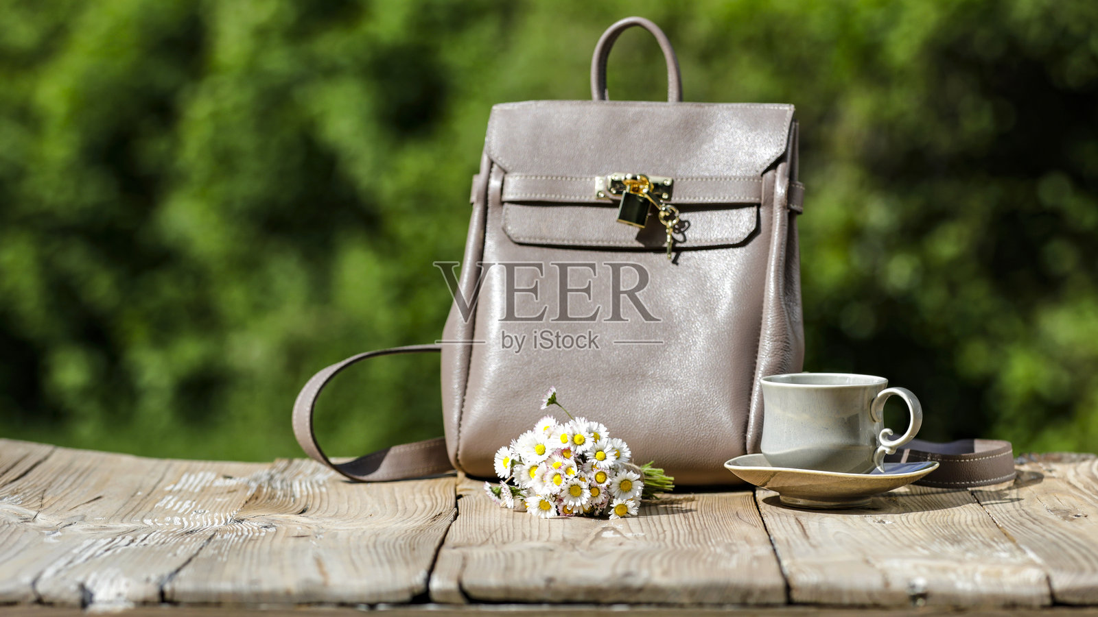 春季构图，木桌上摆放着雏菊花束、杯子、碟子和手袋，背景是模糊的花园。适合母亲节、国际妇女节或贺卡背景，留有空白空间。照片摄影图片