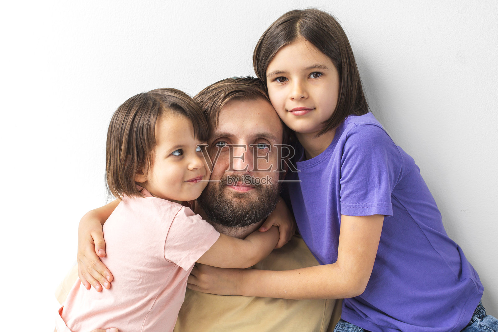 父亲与两个女儿在温馨的家庭时刻中相拥，三人面带平静，紧密相依，背景为白色，体现了爱、联系和育儿的概念。照片摄影图片