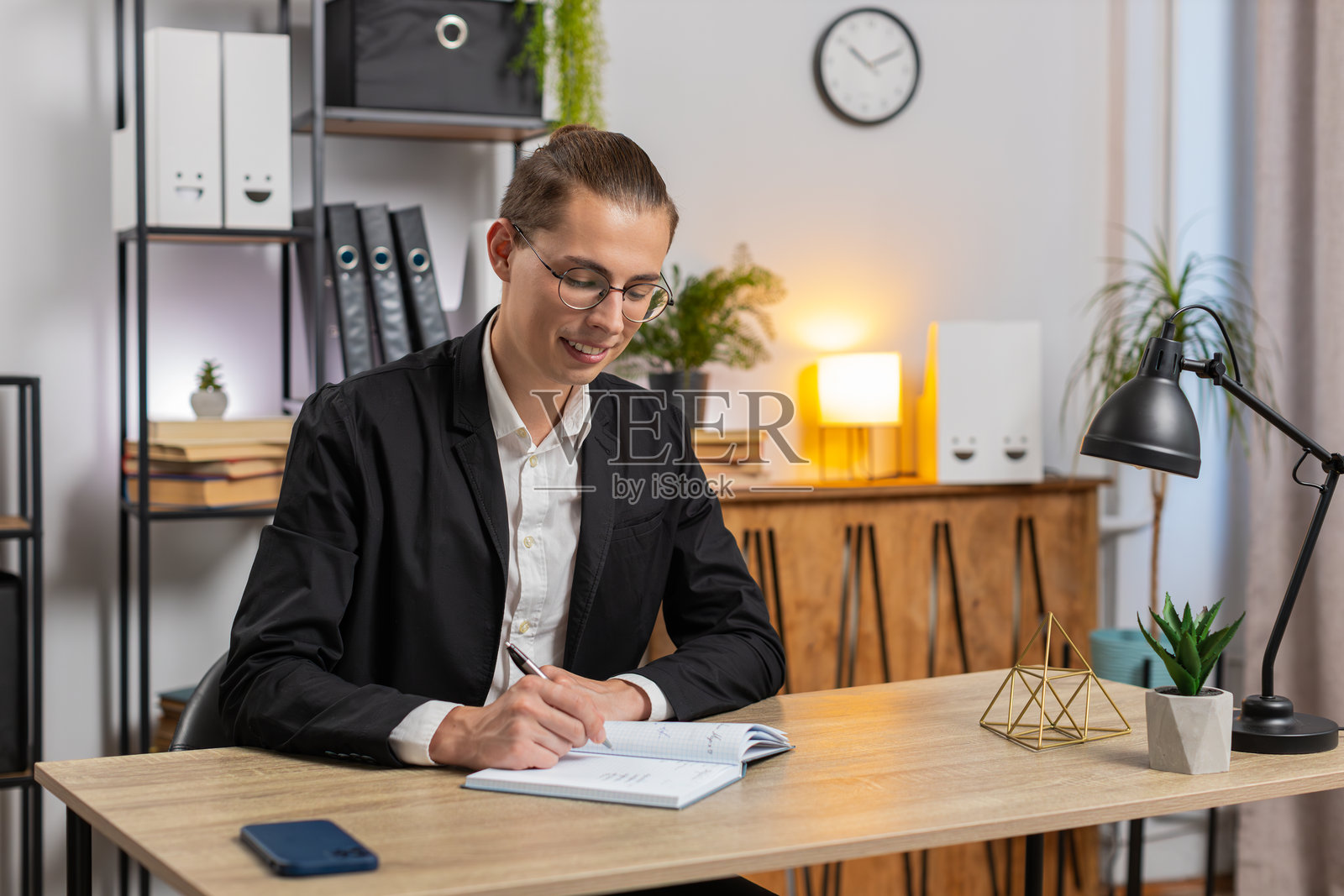 年轻的商人对着镜头微笑，并在家中办公室的桌子上写日记进行视频聊天。照片摄影图片