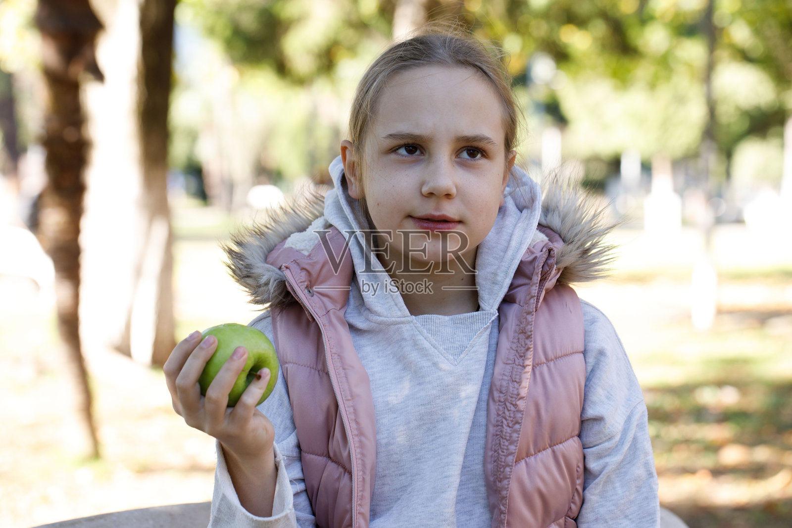 顽皮的孩子手里拿着绿色苹果。公园里的年轻女孩，户外肖像。照片摄影图片