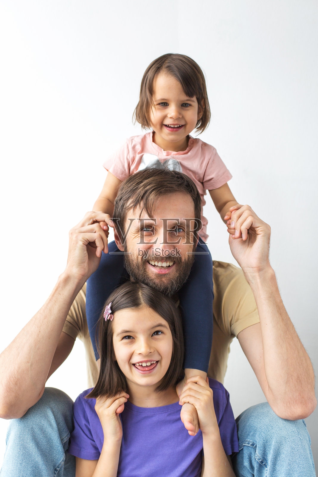 白人父亲与两个微笑的女儿一起合影，年轻的女孩坐在他的肩膀上，展现家庭、父母和童年的概念，背景为白色，竖版。照片摄影图片