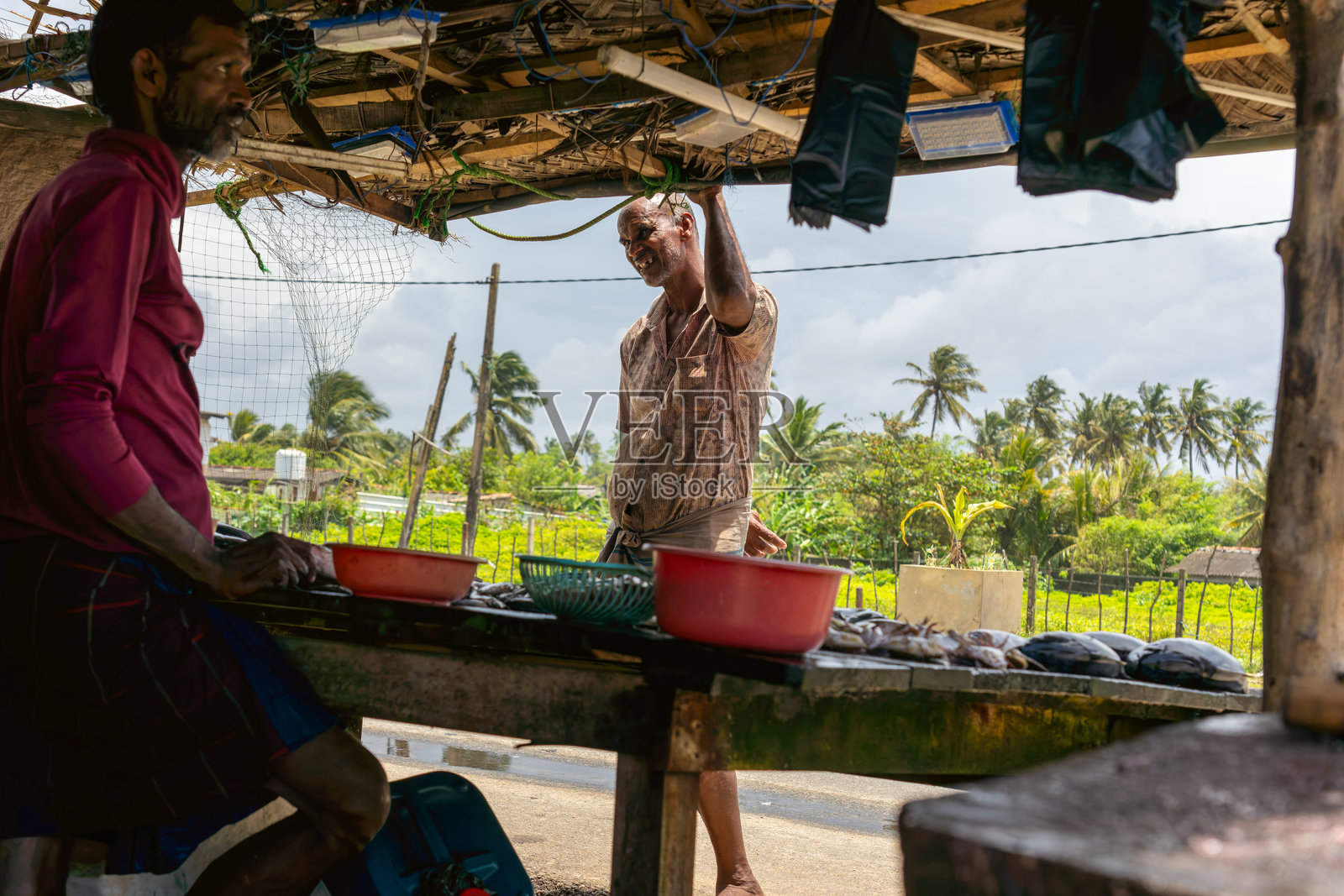 海滩边的街道上，鱼市摊位在棕榈叶屋顶下排成一排。照片摄影图片