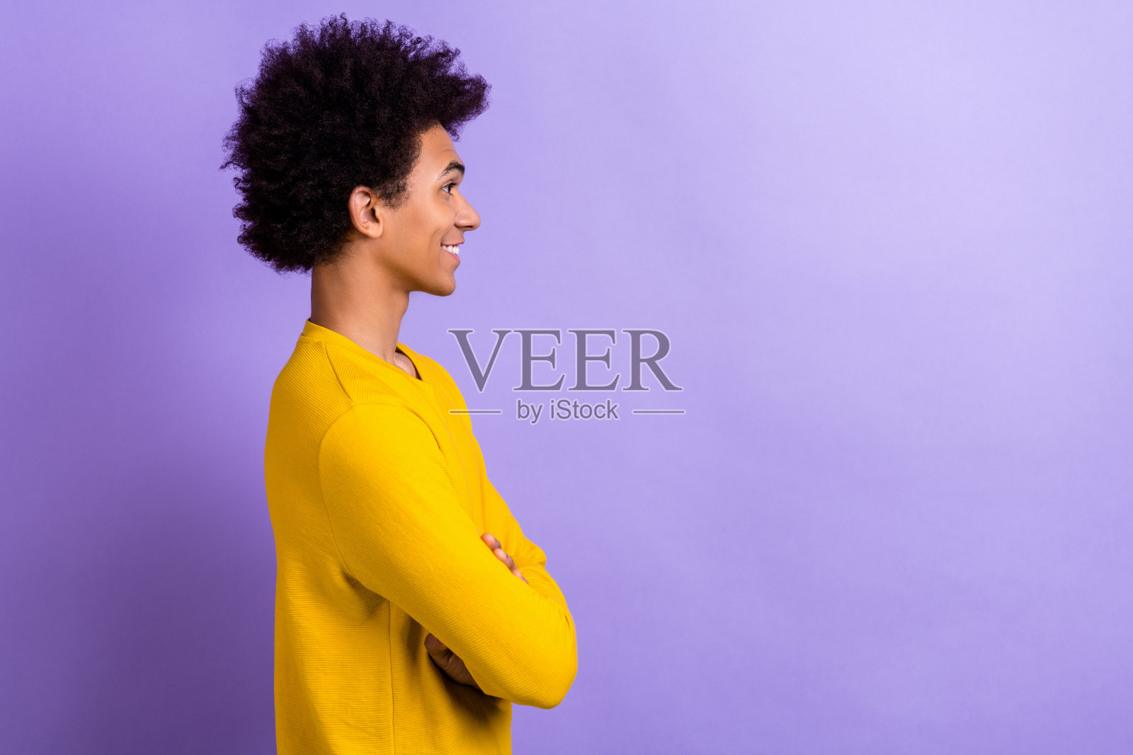 满意的男士侧面照片，穿着黄色长袖，双臂交叉，背景为紫色，显得空旷。照片摄影图片