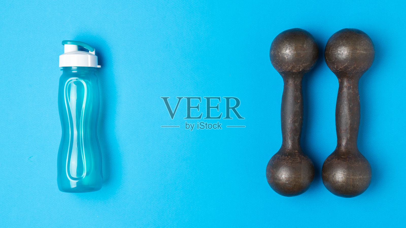 健身必备：蓝色背景下的水瓶和哑铃，展现健康生活方式照片摄影图片