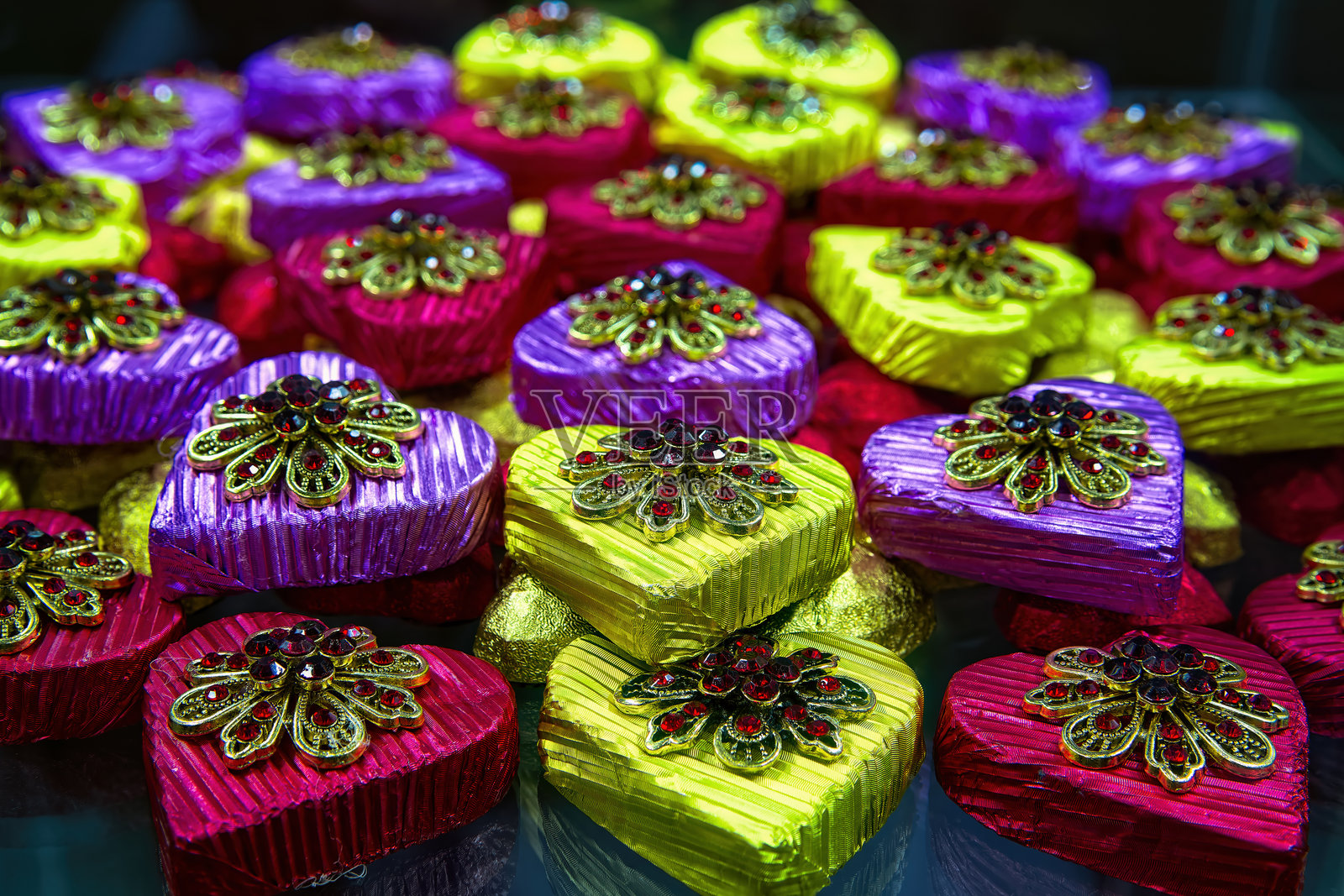 五彩缤纷的心形巧克力糖果，包裹在闪亮的包装纸中，配有礼品胸针，俯视图。照片摄影图片