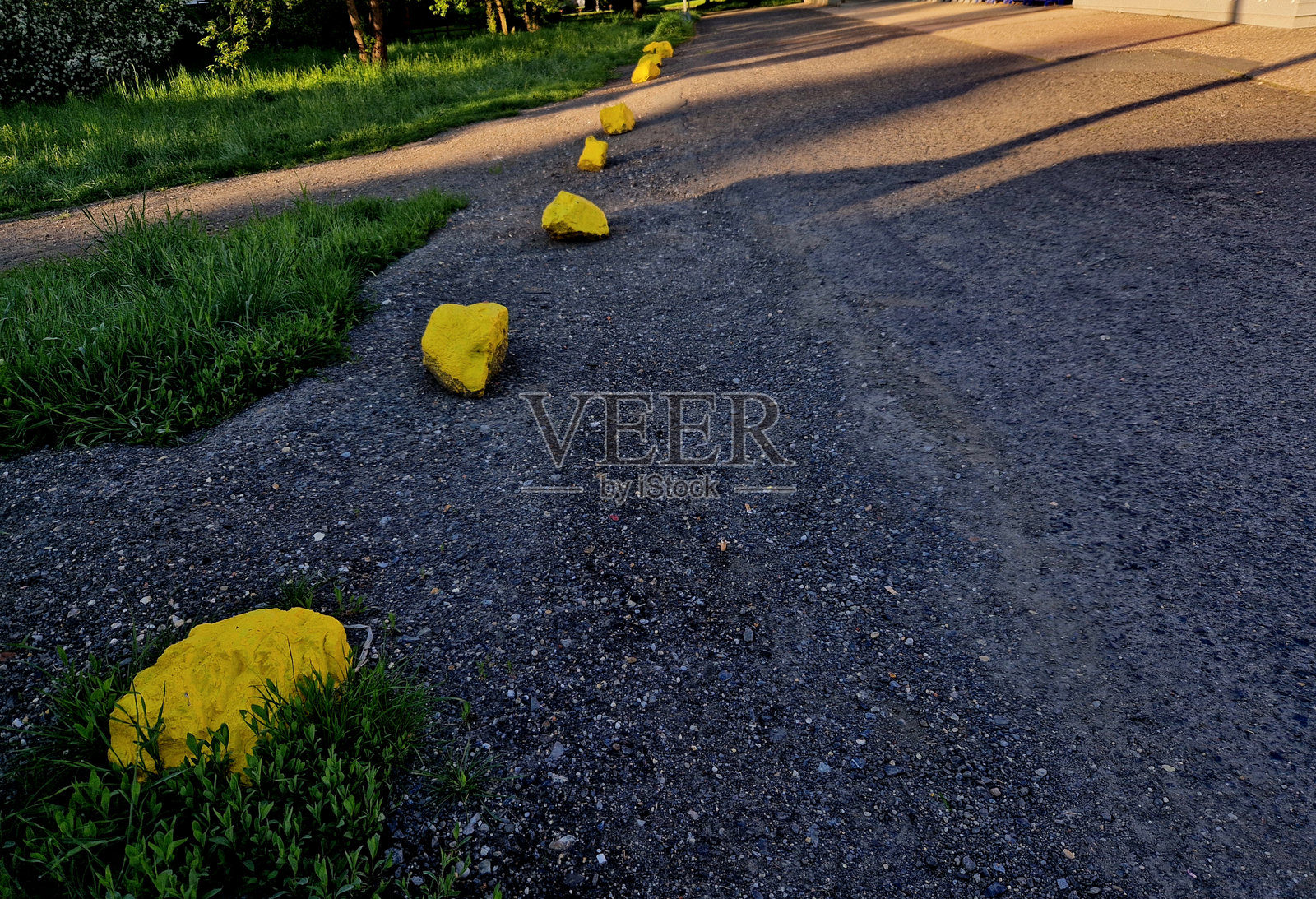 车道之间的灰色石头作为停车保护。乡间道路和自行车道的停车场交通解决方案。沥青表面和草坪，锁定金属柱。红色条纹。照片摄影图片