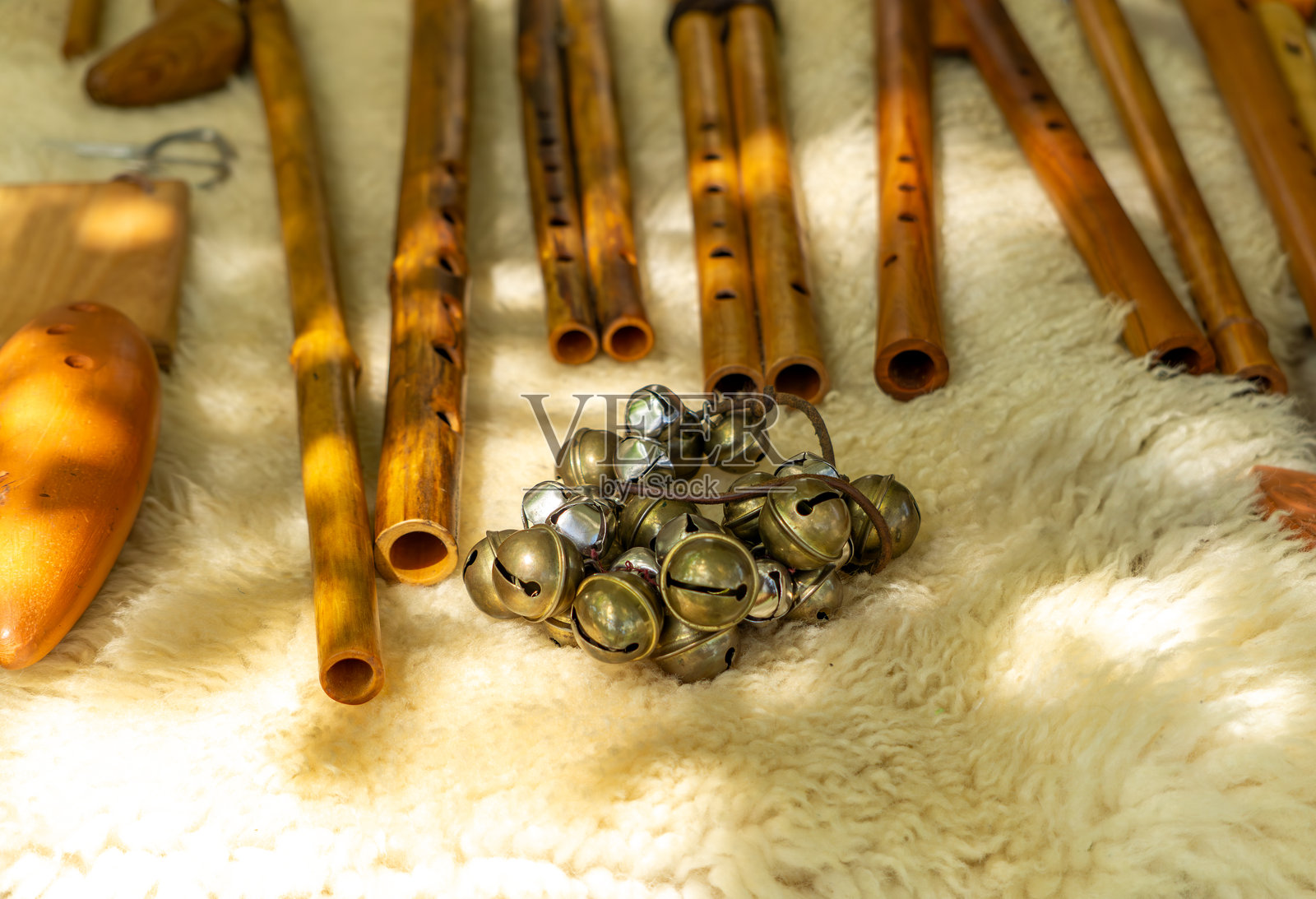 一组木制长笛和铃铛的特写，放置在白色毛皮上。传统乐器在自然光下拍摄，完美展示民间传说、民族音乐或手工艺品。照片摄影图片
