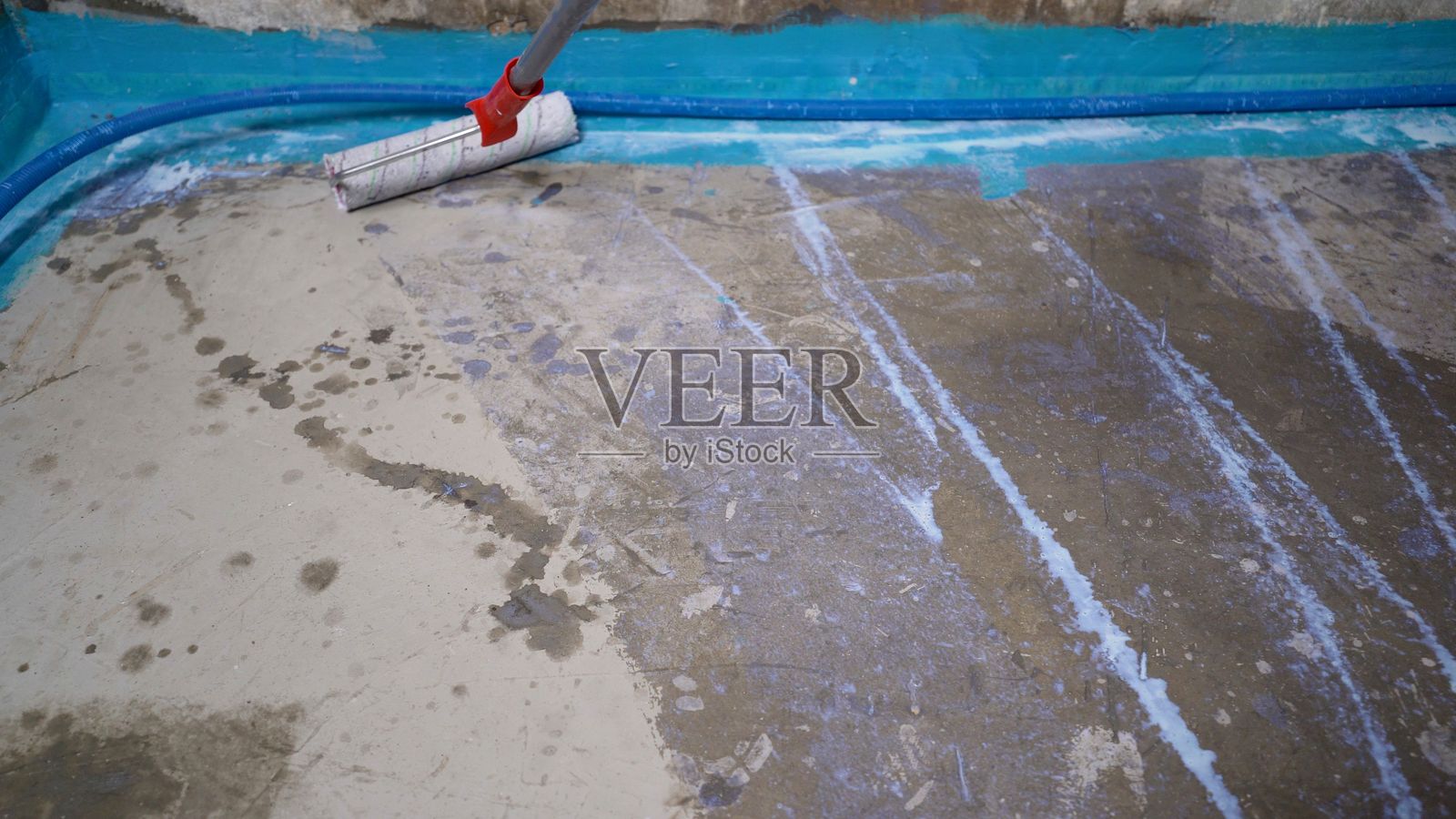 建筑工人在混凝土地面上使用滚筒涂抹防水膜照片摄影图片