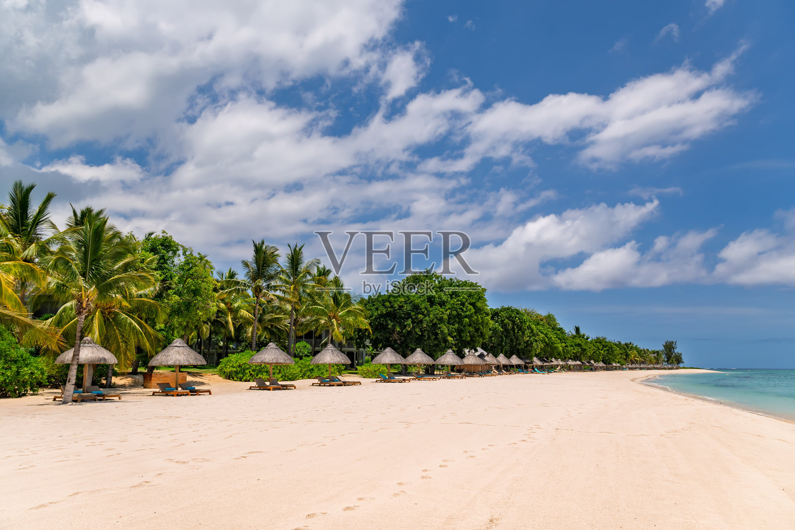 隐秘的热带度假村海滩，配有茅草伞和清澈的蓝色海水。宽广的白色沙滩，设有海滩小屋和碧绿色的海水。照片摄影图片