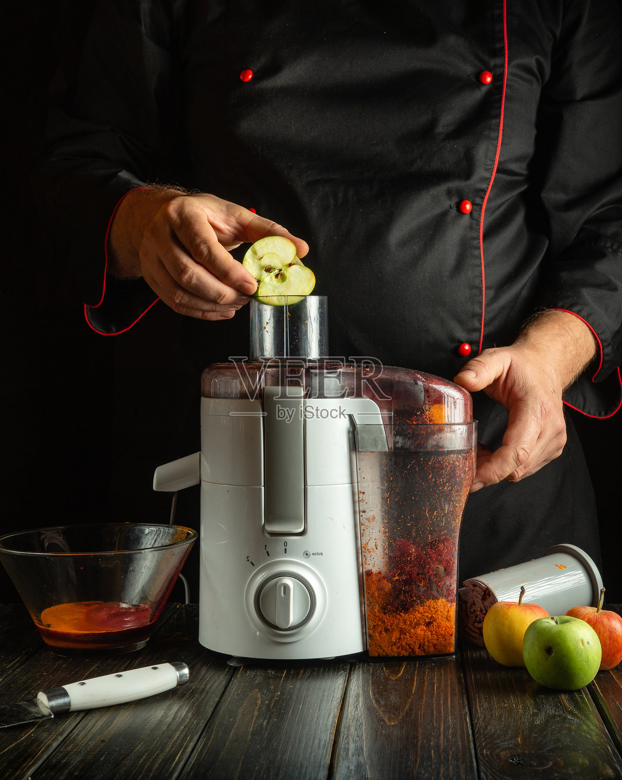 一位熟练的厨师正在将苹果片放入榨汁机中准备新鲜果汁。温暖的厨房里充满了水果，营造出一个舒适的晚间氛围。照片摄影图片