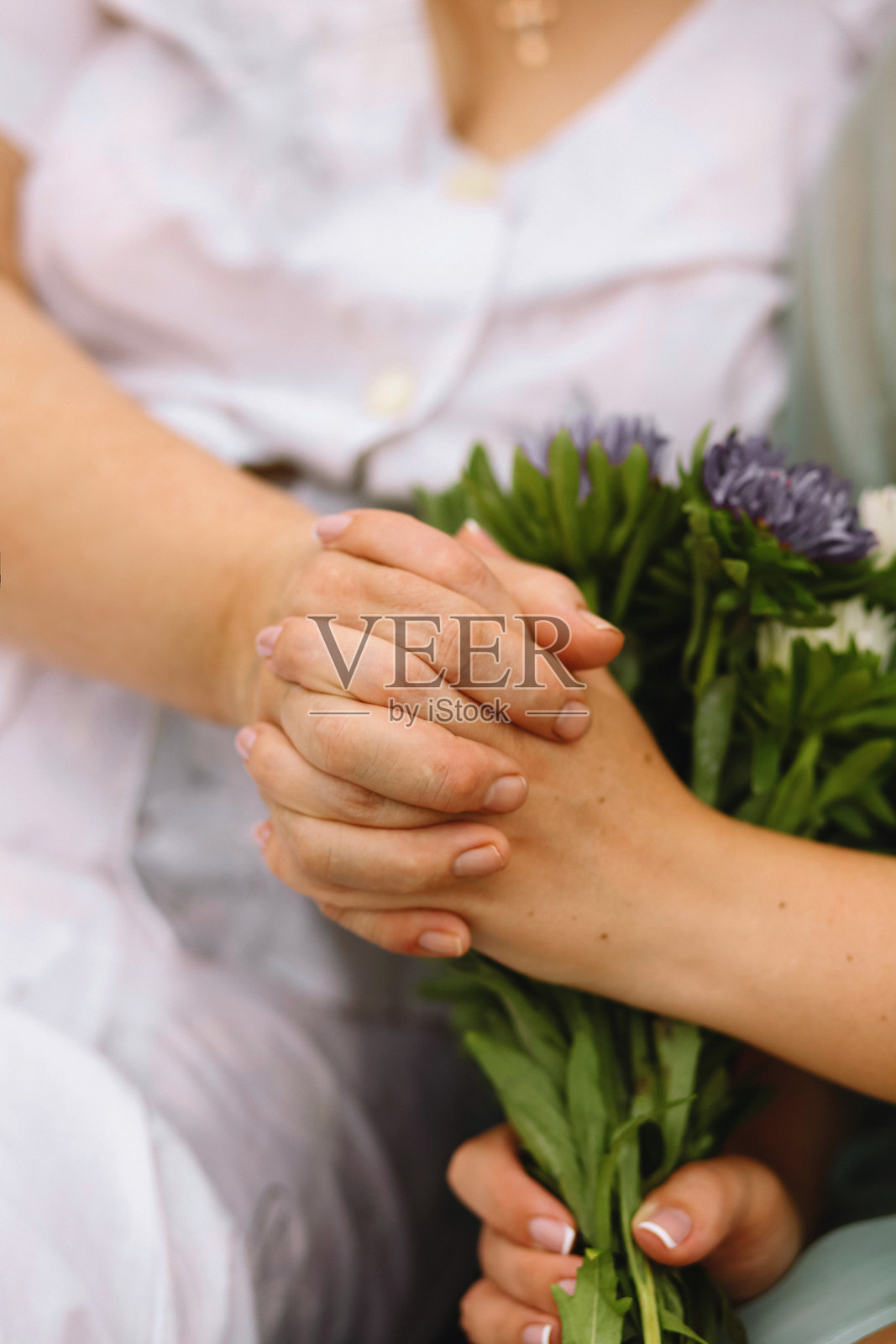 年轻的手握着一只老年的手，夏天的大自然中。母女互相握着手。家庭概念。照片摄影图片