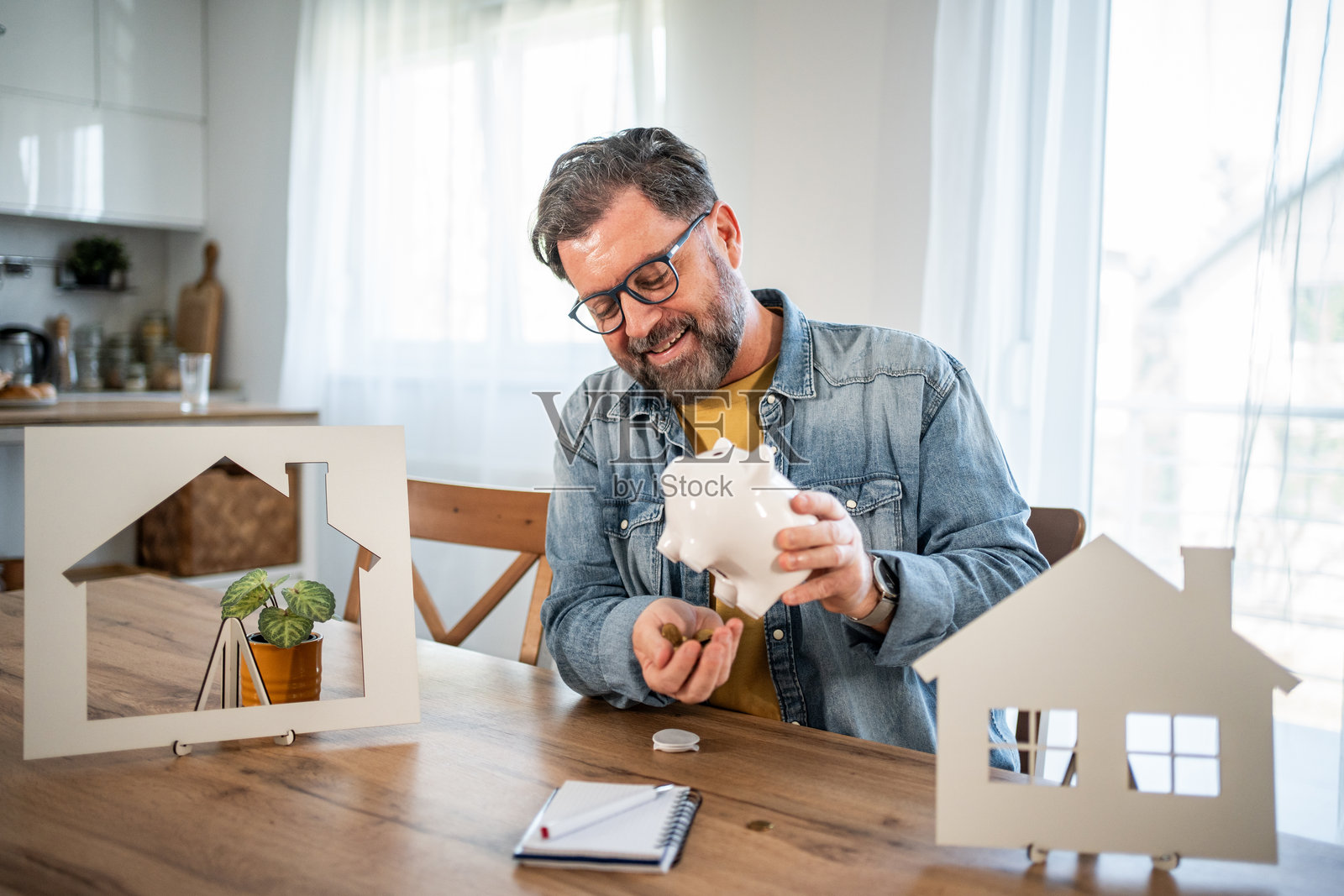 中年男子在储蓄罐里存钱以购买新家照片摄影图片
