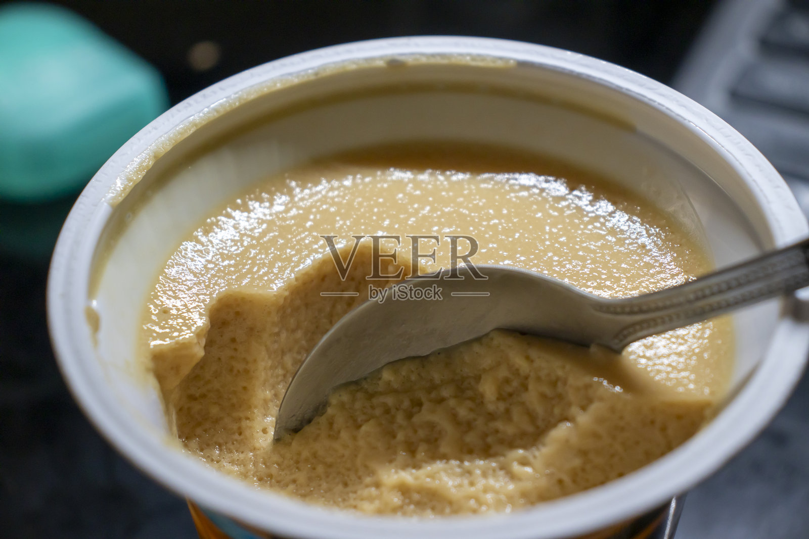 碗中盛着奶油甜点，配有银色勺子，随时可以享用。非常适合烹饪概念。光滑的质地和丰富的色彩唤起一种奢华感。照片摄影图片