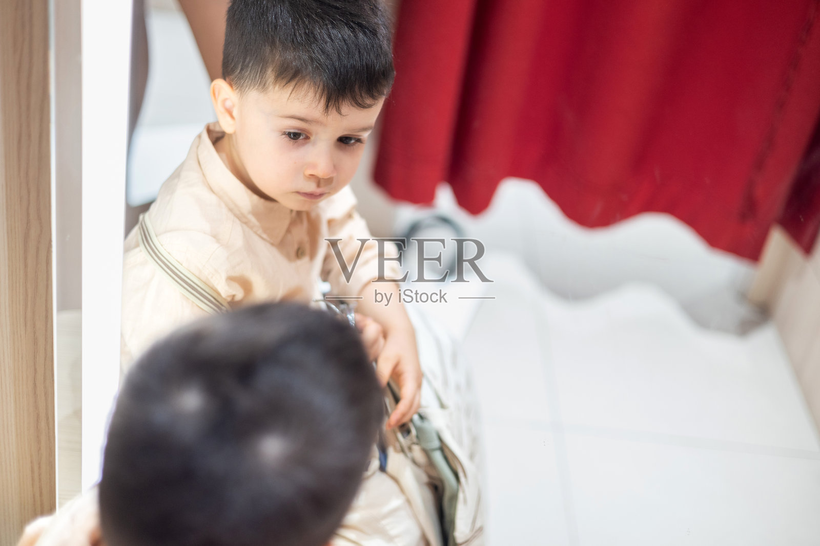 孩子在试衣间试穿衣服。男孩手里拿着一堆衣物坐在椅子上。可爱的孩子在镜子前做搞笑表情。微笑的宝宝在购物中心，商场里。照片摄影图片