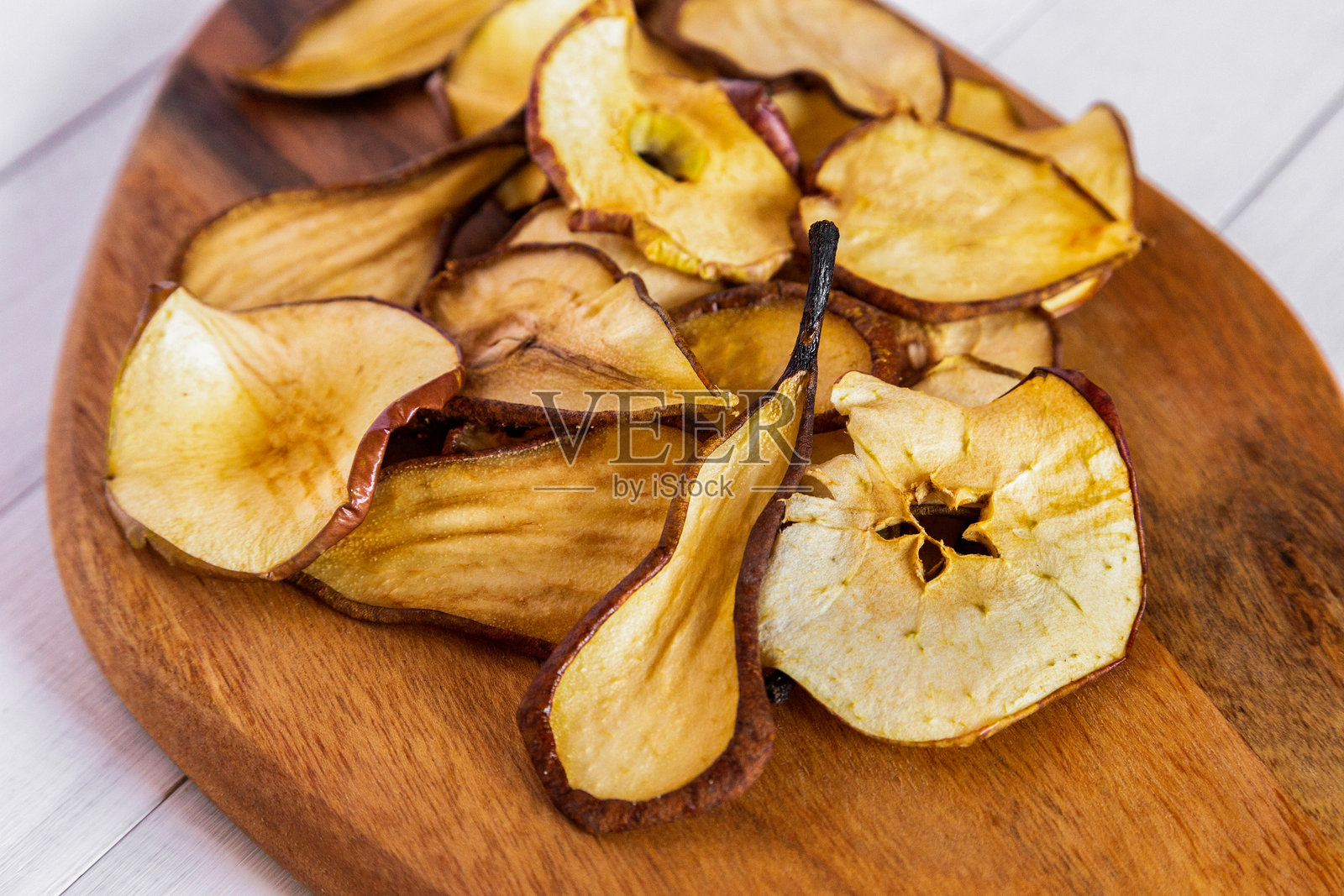 特写镜头展示了干燥的梨片和苹果片，放在木质椭圆形砧板上，突显了质感和自然细节。照片摄影图片