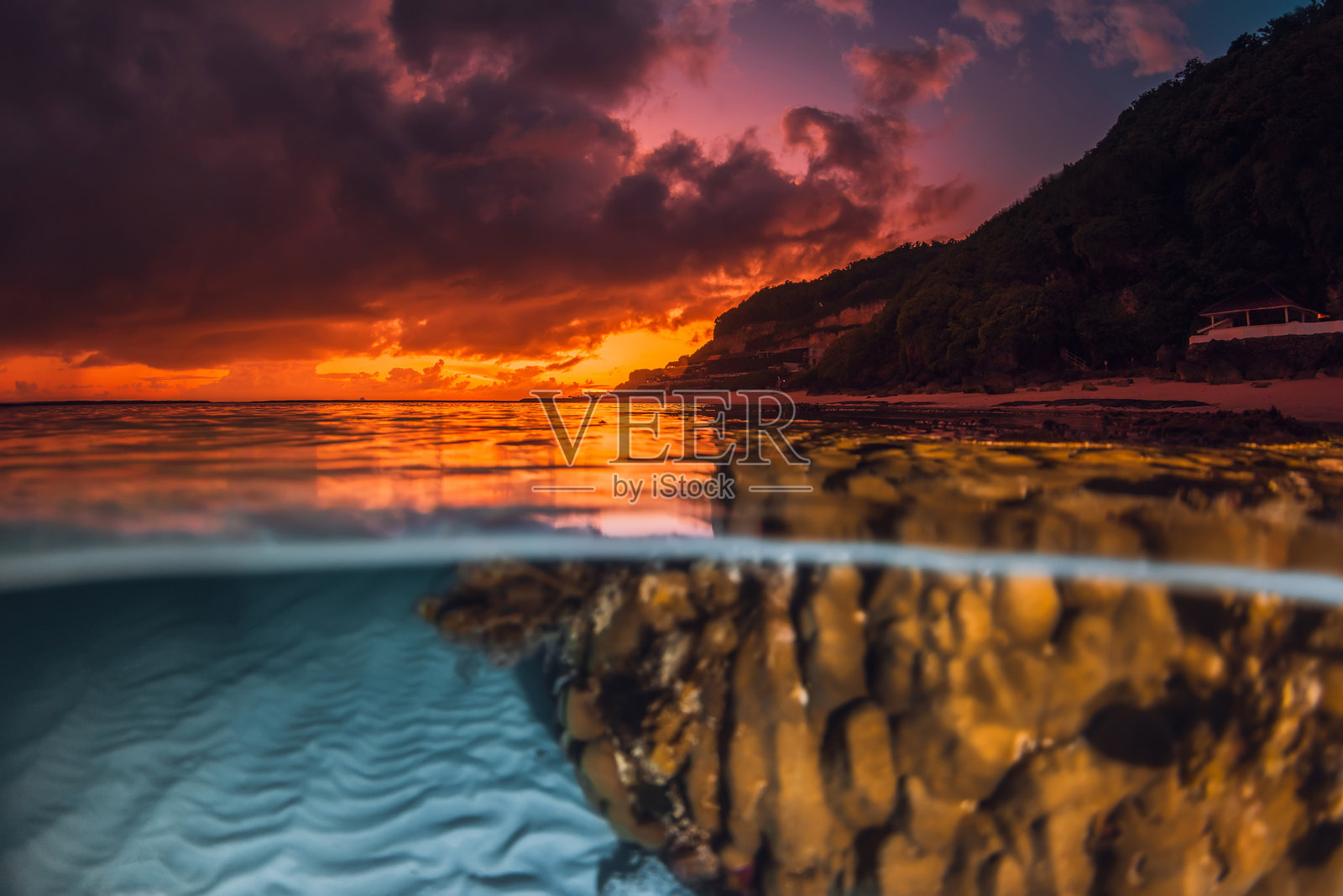 戏剧性的日落或日出映照在平静的海面上，水下沙子图案和珊瑚清晰可见，呈现出分层视角的海景。照片摄影图片