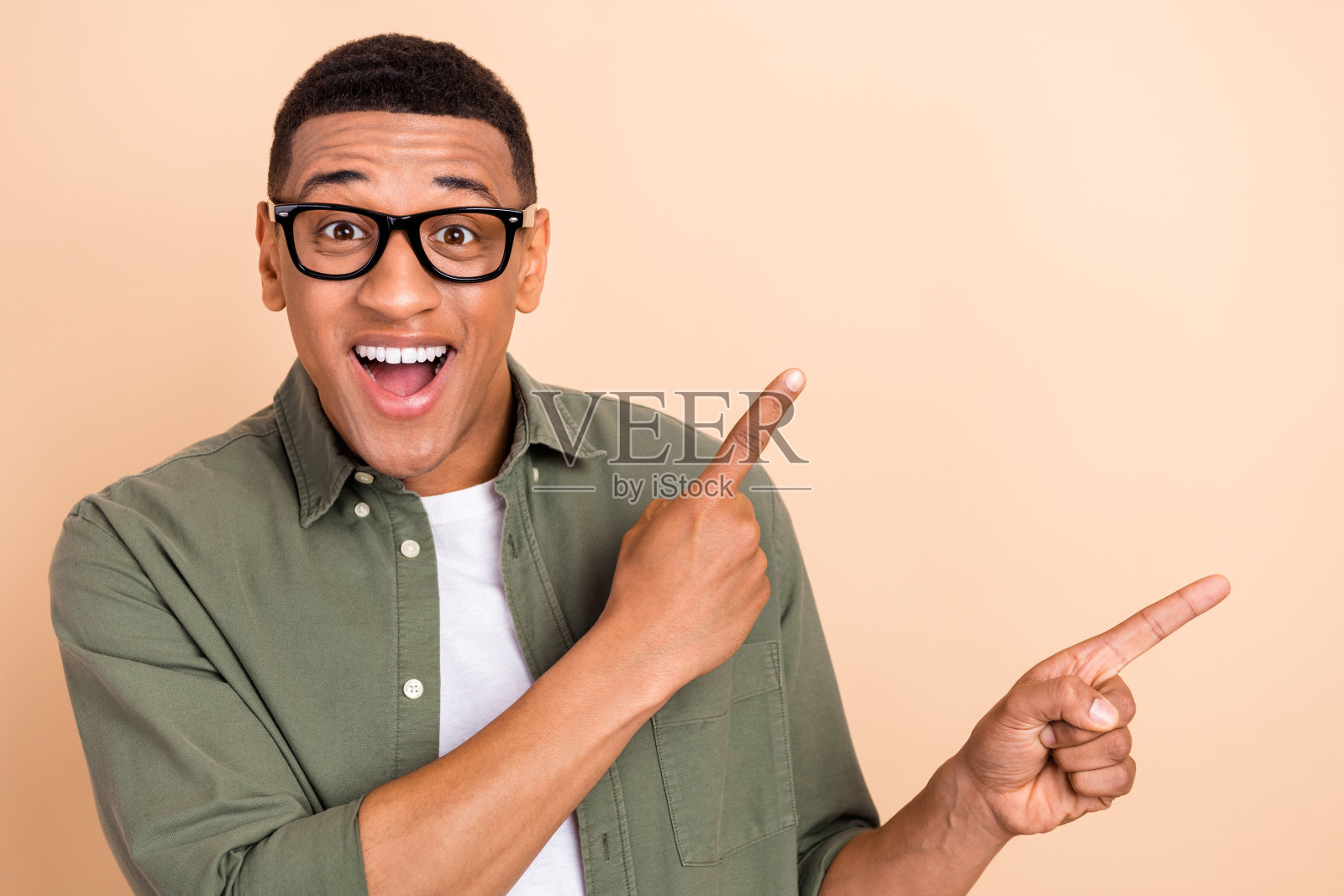 惊讶的积极男性肖像，张嘴用手指指向空白信息区域，背景为米色。照片摄影图片