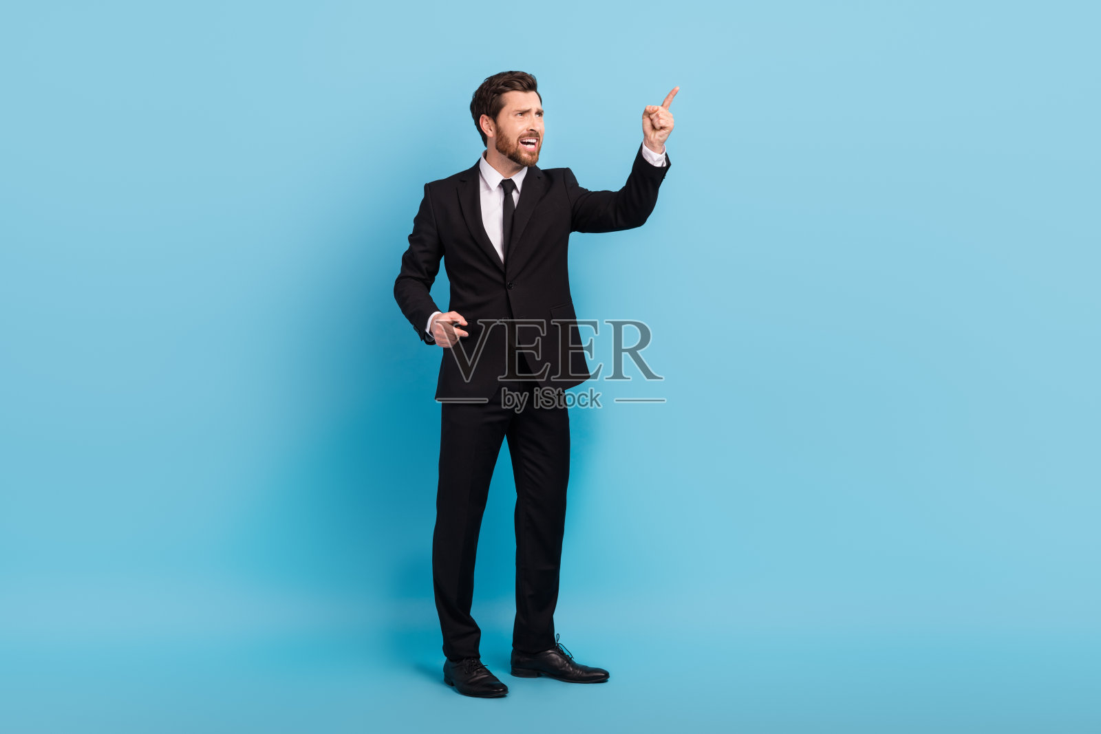 穿着黑色西装的愤怒老板在蓝色背景下尖叫并指向空旷的地方的全身照片照片摄影图片