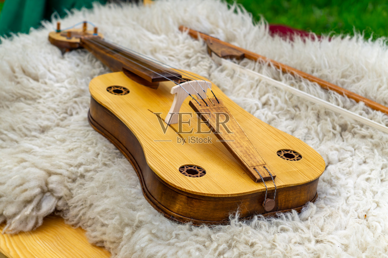传统木制民间乐器的特写 — 一把弓弦小提琴 — 静静地放在白色毛皮上。手工制作的细节在自然光下熠熠生辉，完美展现民俗文化、早期音乐和传统工艺。照片摄影图片