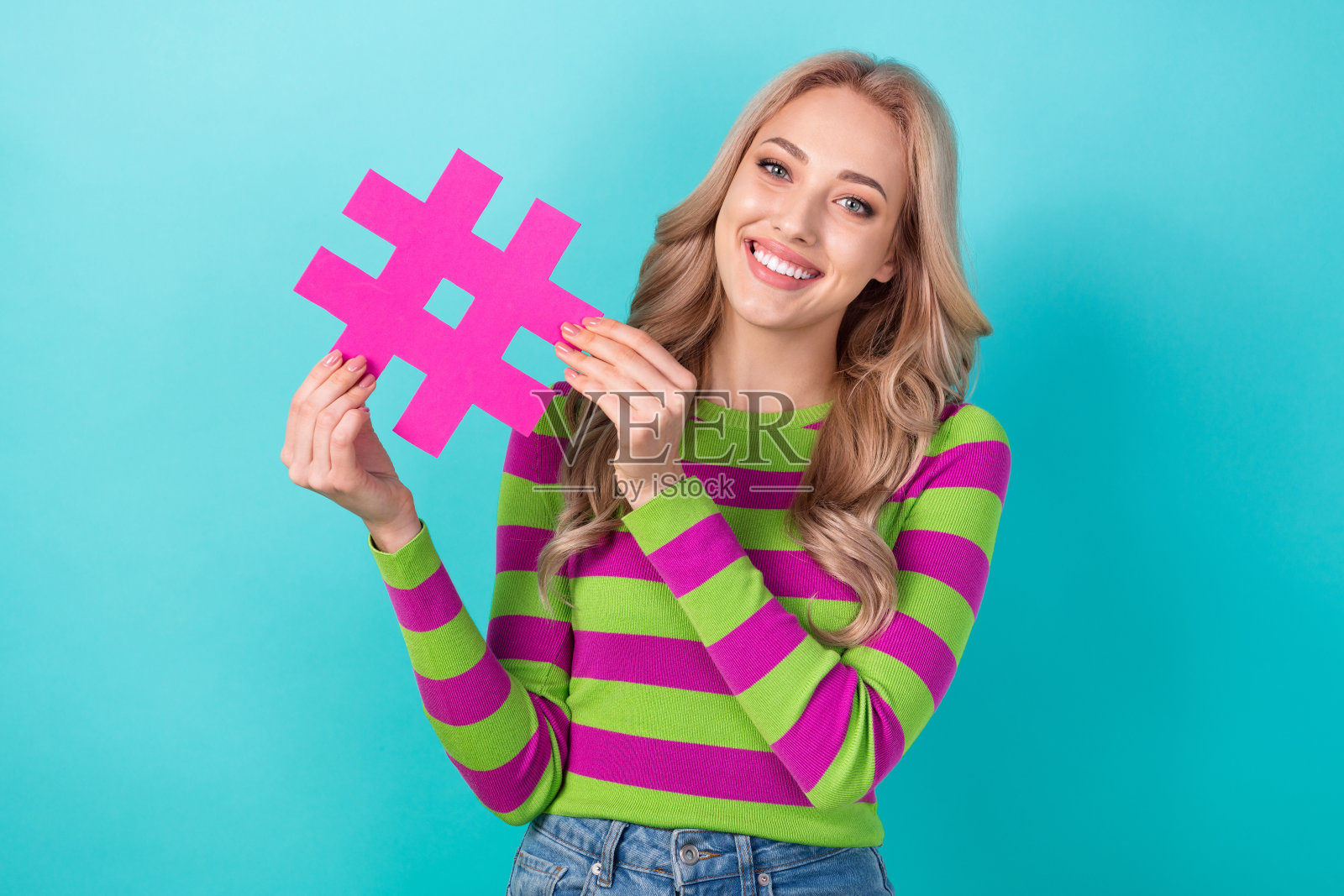 漂亮年轻女孩的照片肖像，手持粉色的社交媒体经理标签，穿着时尚的条纹服装，背景为水绿色。照片摄影图片