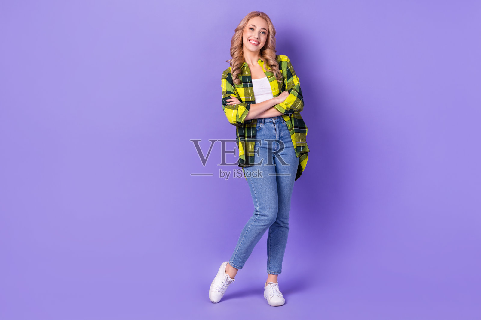 全身照，光彩照人的迷人女性穿着格子夹克，双臂交叉，凝视空旷的空间，背景为紫色。照片摄影图片