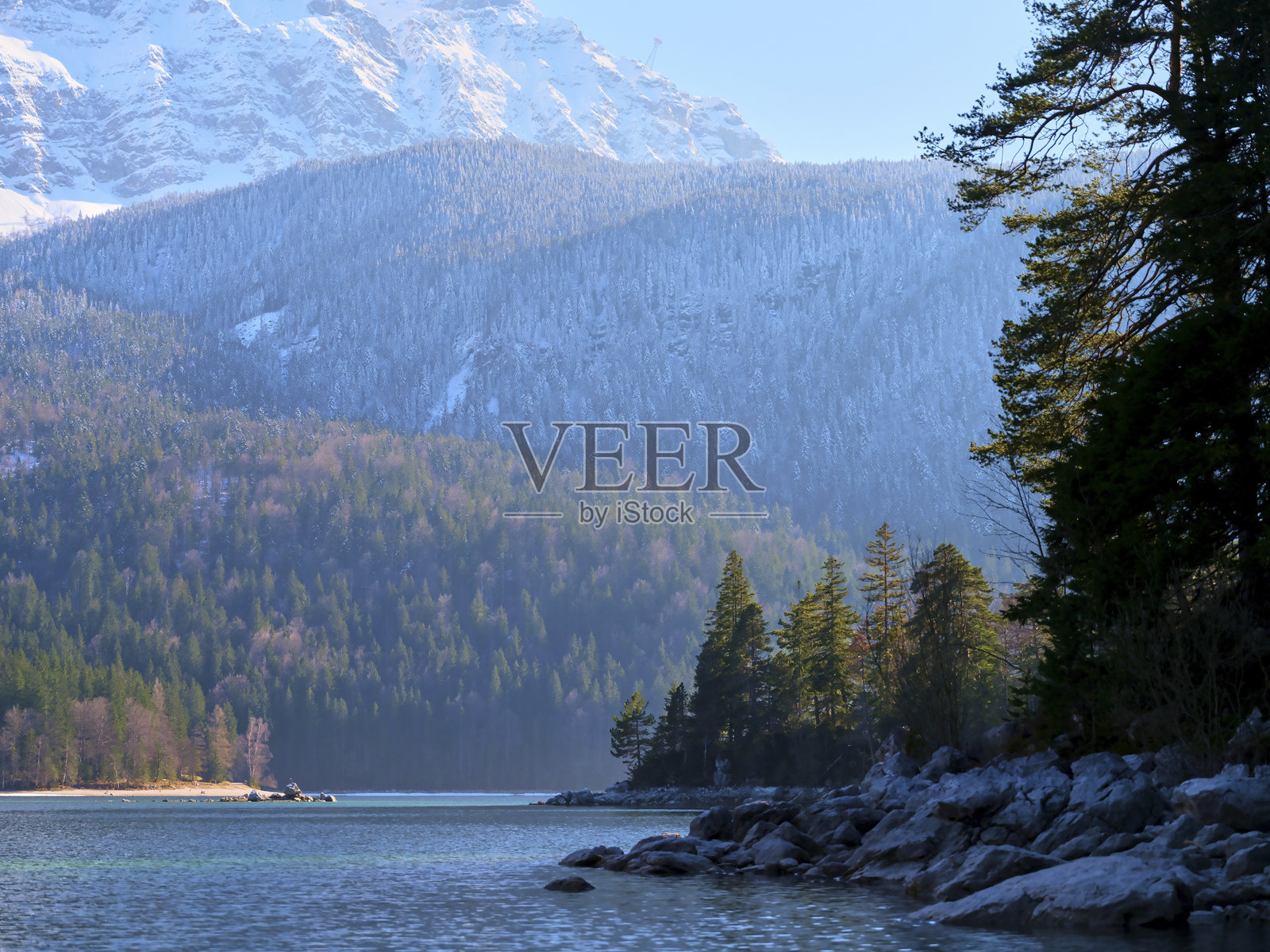 冬季山景，清晨的阳光照耀下，宁静的湖泊被常青树环绕照片摄影图片