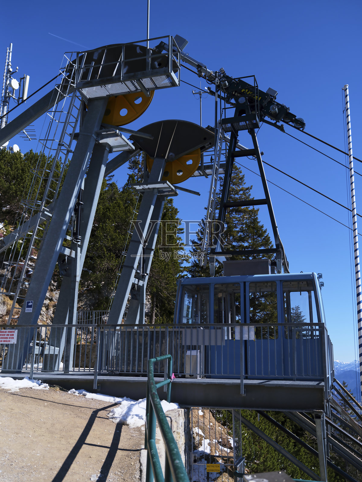 在晴朗的日子里，山地区域的缆车站，周围被雪覆盖，附近有高耸的树木。照片摄影图片