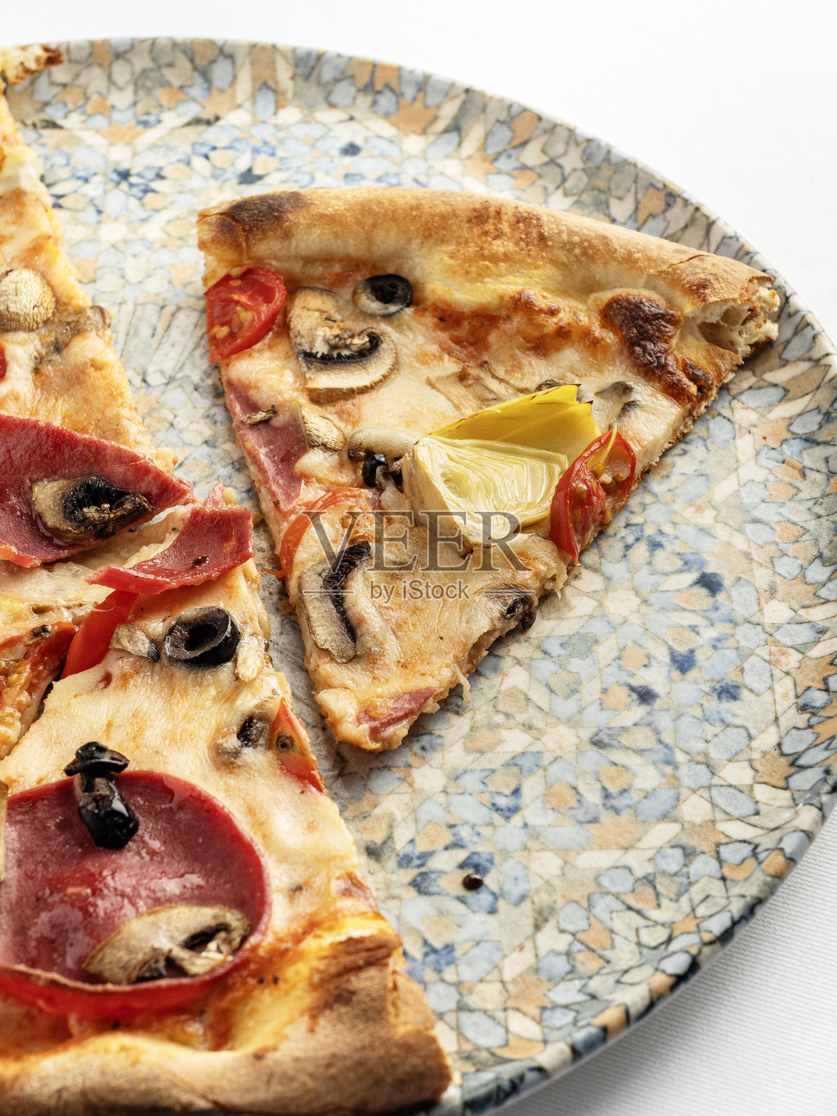 卡普里乔萨披萨。美味的意大利肉类披萨，配有多种配料。白色桌面上的卡普里乔萨披萨，上面有朝鲜蓟、蘑菇和苏贾克香肠。披萨照片摄影图片