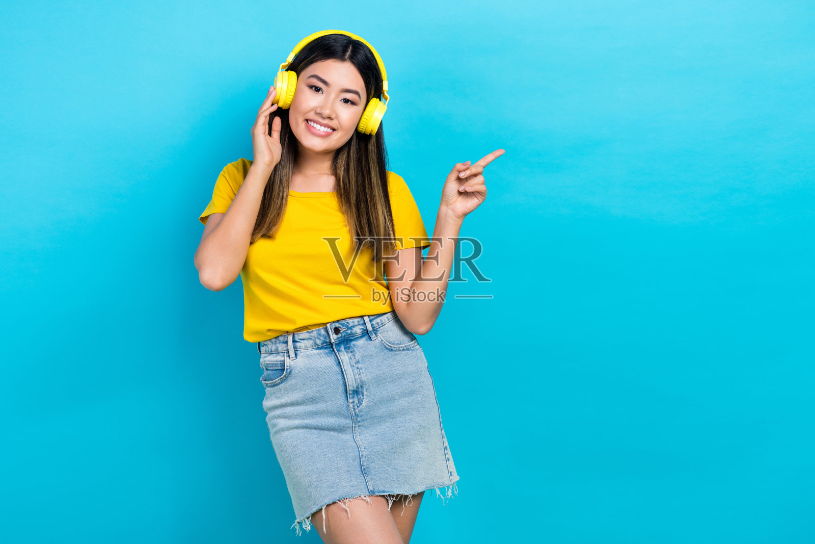 迷人的积极人物触摸耳机，用手指指向空白空间，背景为蓝色。照片摄影图片