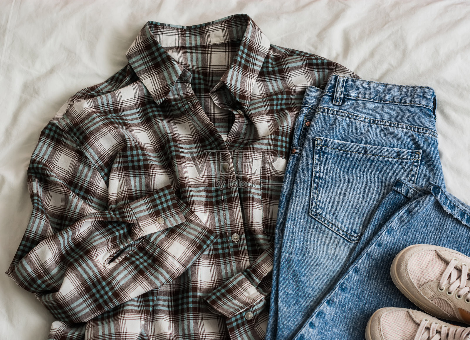 女性服装 - 格子衬衫、蓝色牛仔裤、白色运动鞋，浅色背景，俯视图照片摄影图片