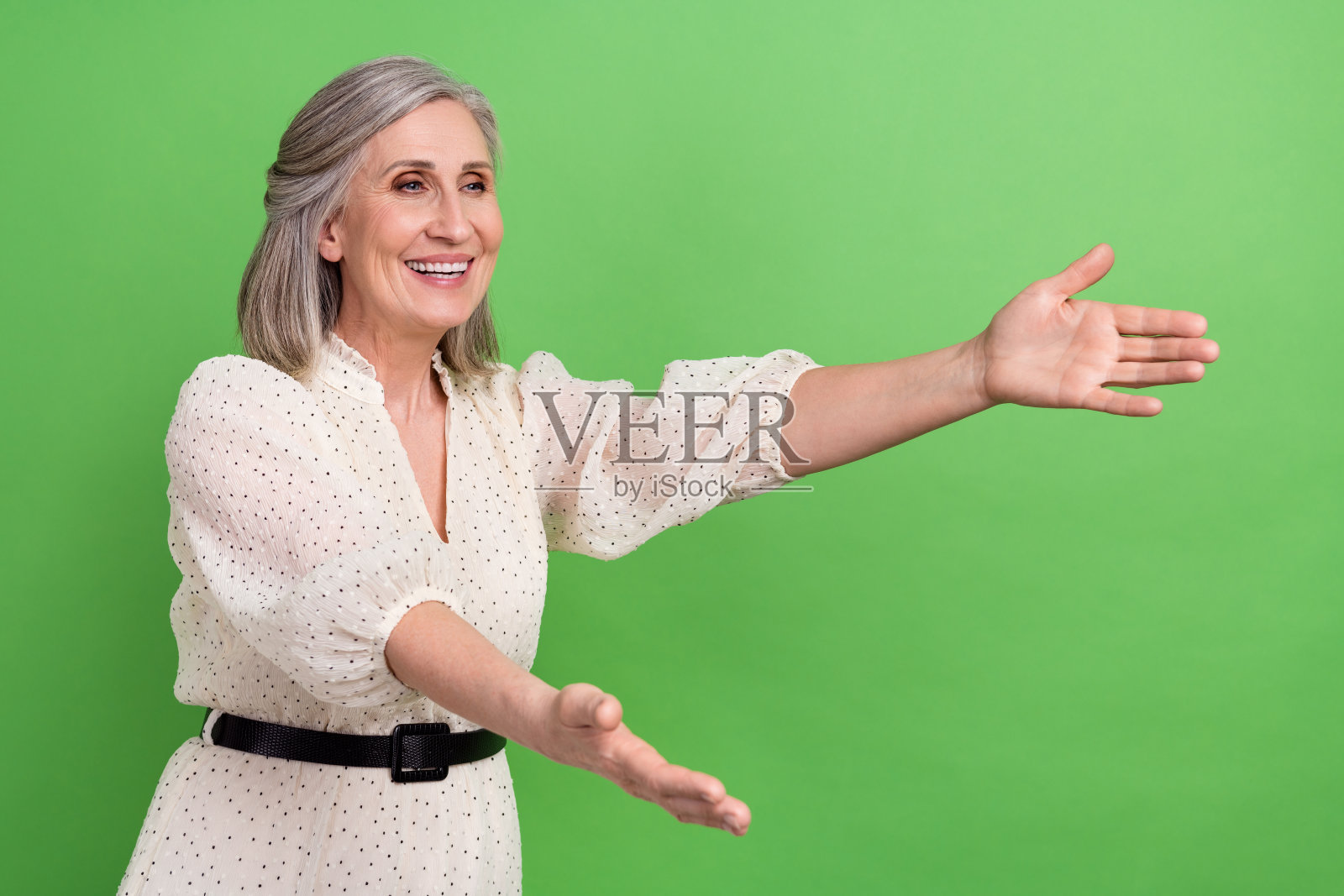 穿着米色裙子的积极兴奋的女士在绿色背景下张开双臂，仿佛在捕捉掉落的空中。照片摄影图片